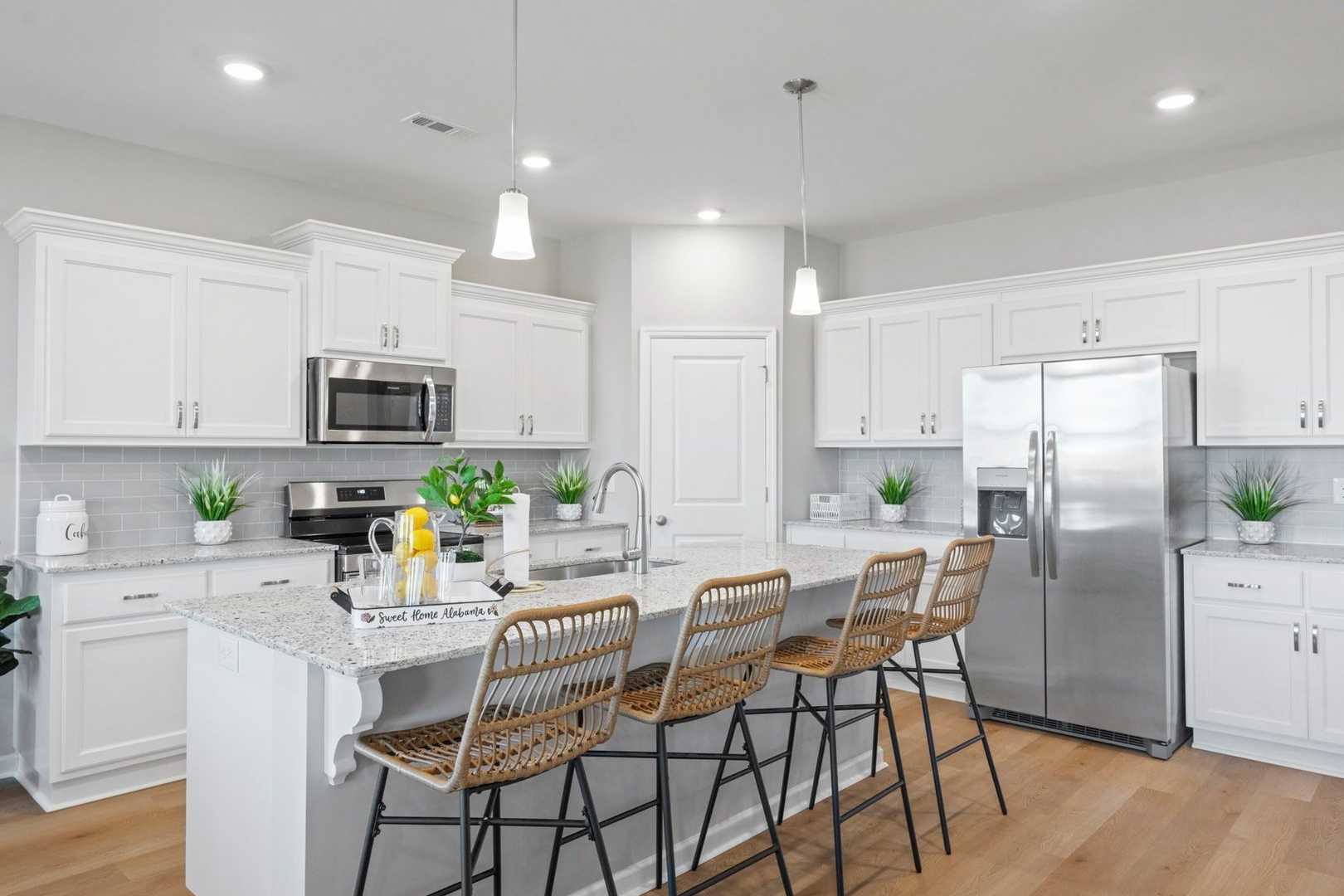 Spacious white kitchen in The Phoenix with large island, wicker bar stools, stainless steel appliances, and potted plants