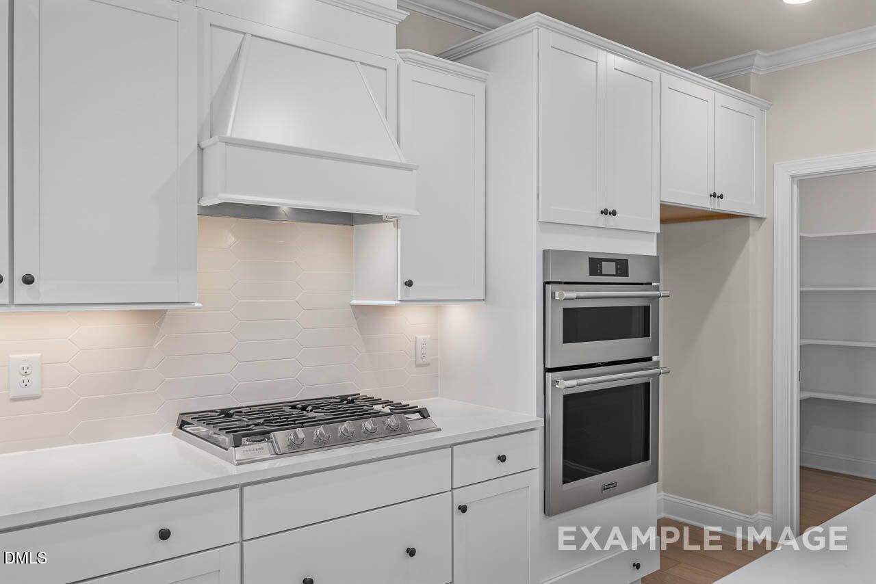 Modern white kitchen featuring stainless double oven, gas cooktop, subway tile backsplash, and pantry in Davidson Homes The Crawford D, Angier, NC