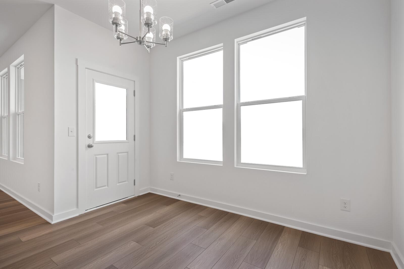 Bright breakfast nook in The Asheville home design with chandelier, large windows, white walls, and hardwood floors