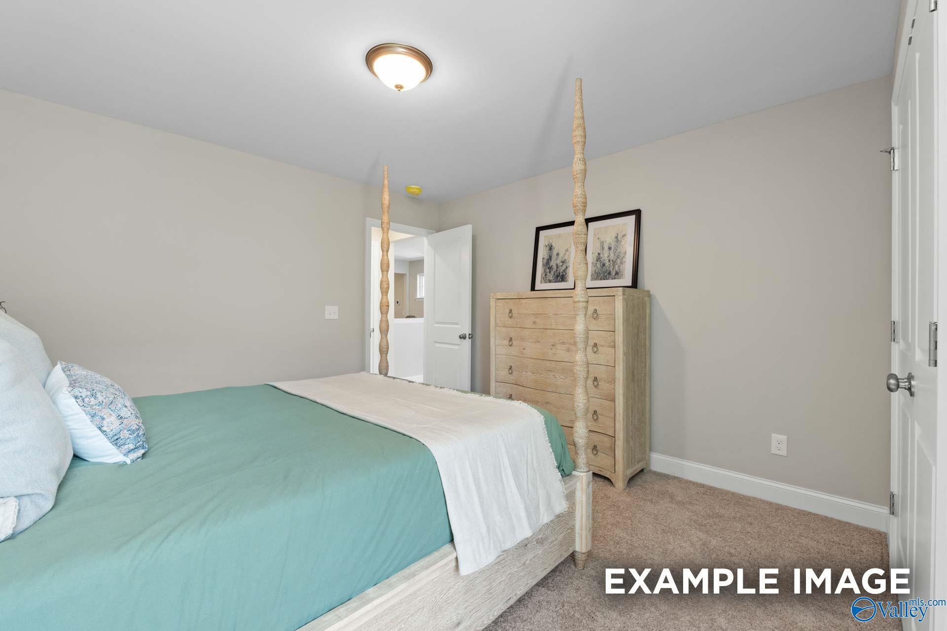 Cozy bedroom with white four-poster bed, teal bedding, wooden dresser and artwork in Evermore Homes The Haven E, Owens Cross Roads, AL