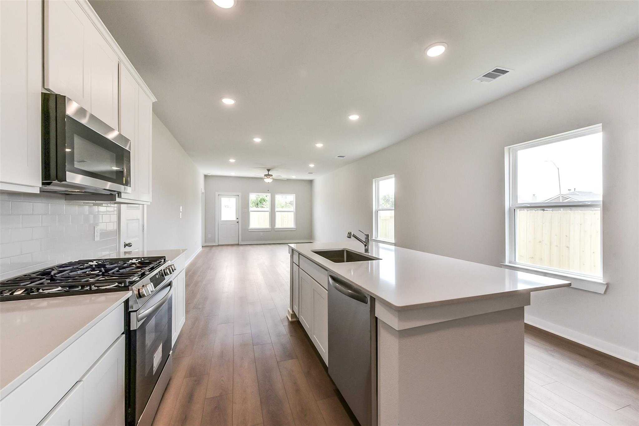 Modern open-concept kitchen with white cabinets, stainless steel appliances, quartz island sink in Davidson Homes The Frio F, Dayton, Texas