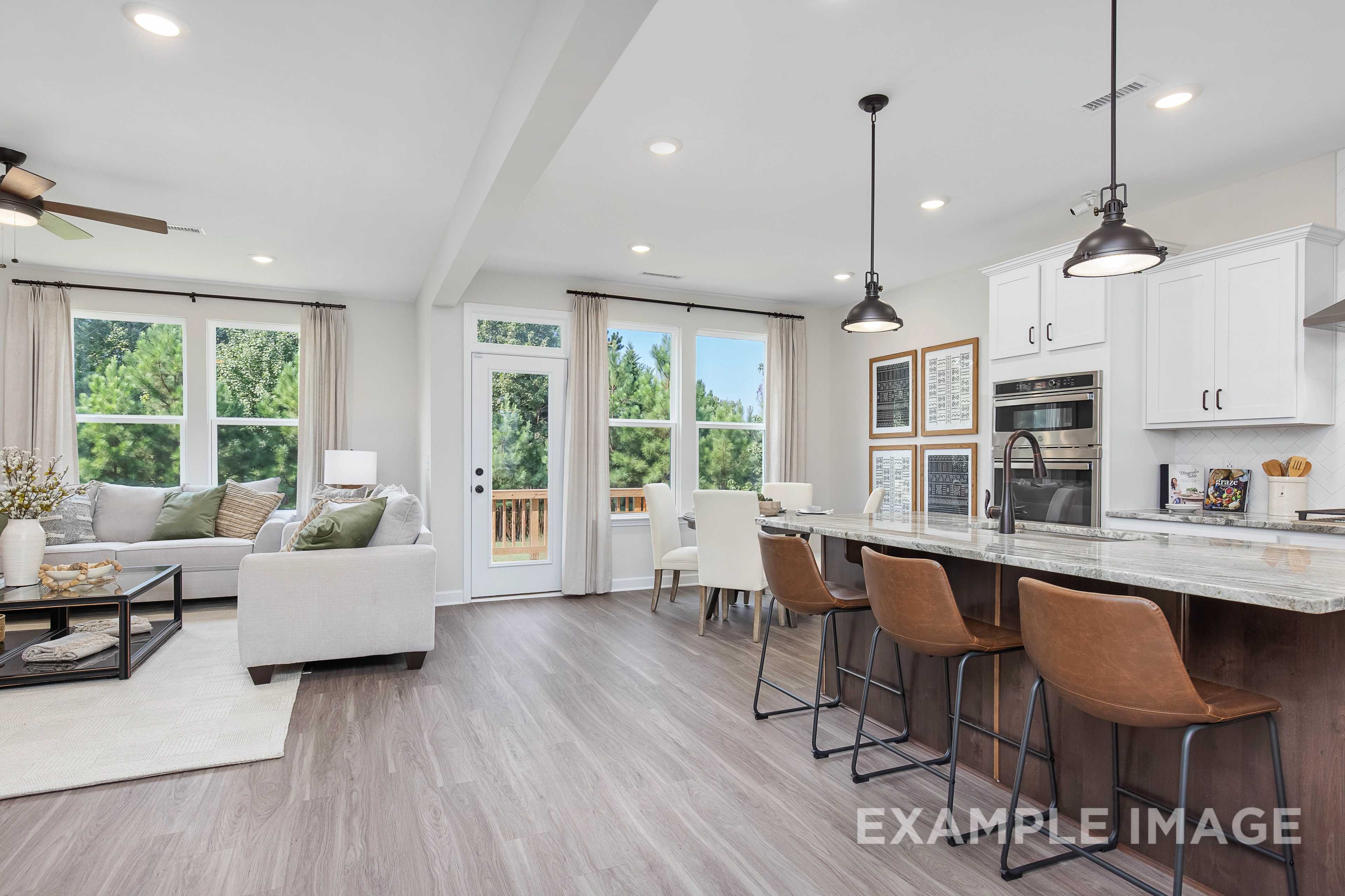 Spacious open-concept kitchen and living room in The Willow B with white cabinets, quartz island, and large windows