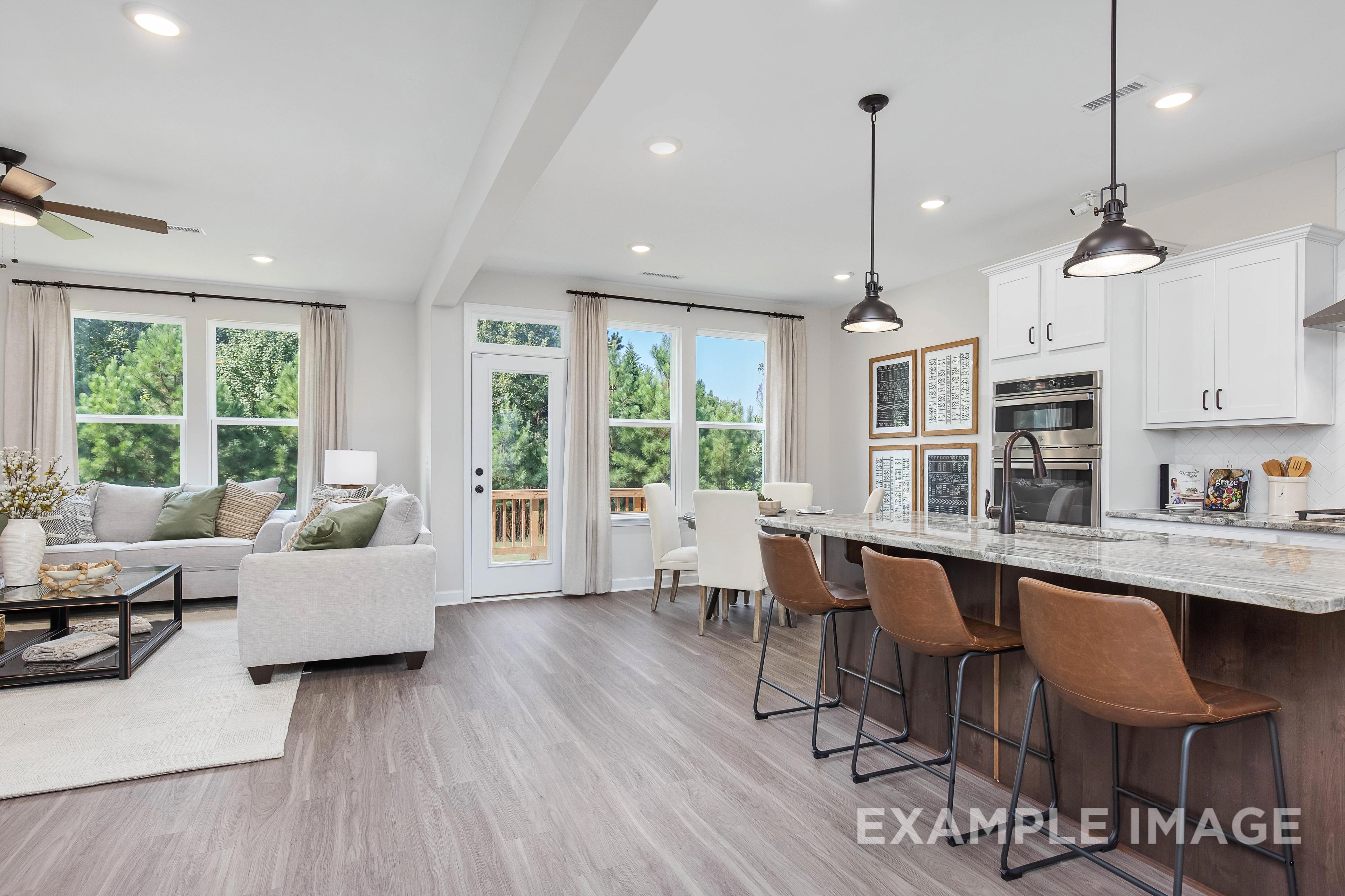 Spacious open-concept kitchen and living room in The Willow B with white cabinets, quartz island, and large windows