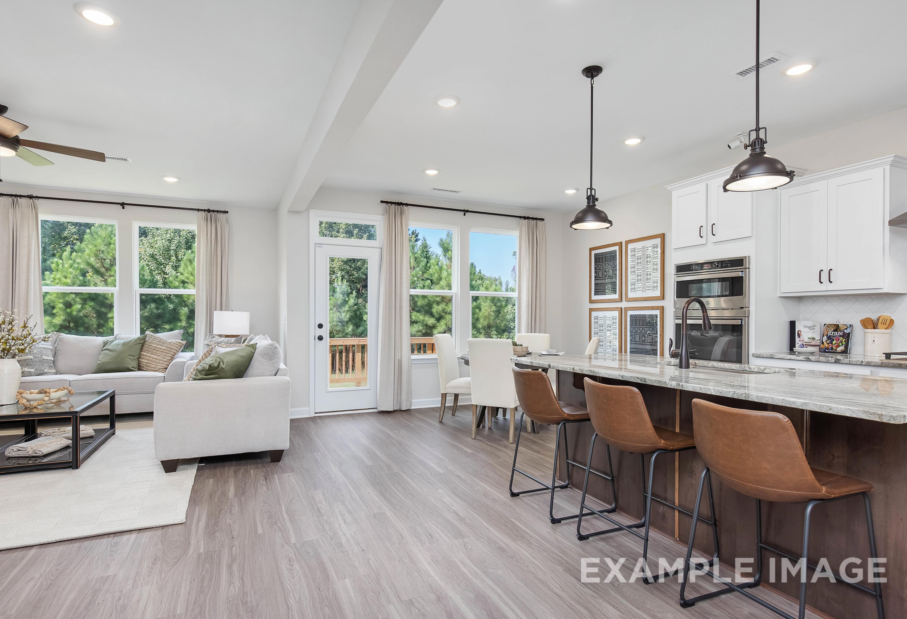 Spacious open-concept kitchen and living room in The Willow B with white cabinets, quartz island, and large windows
