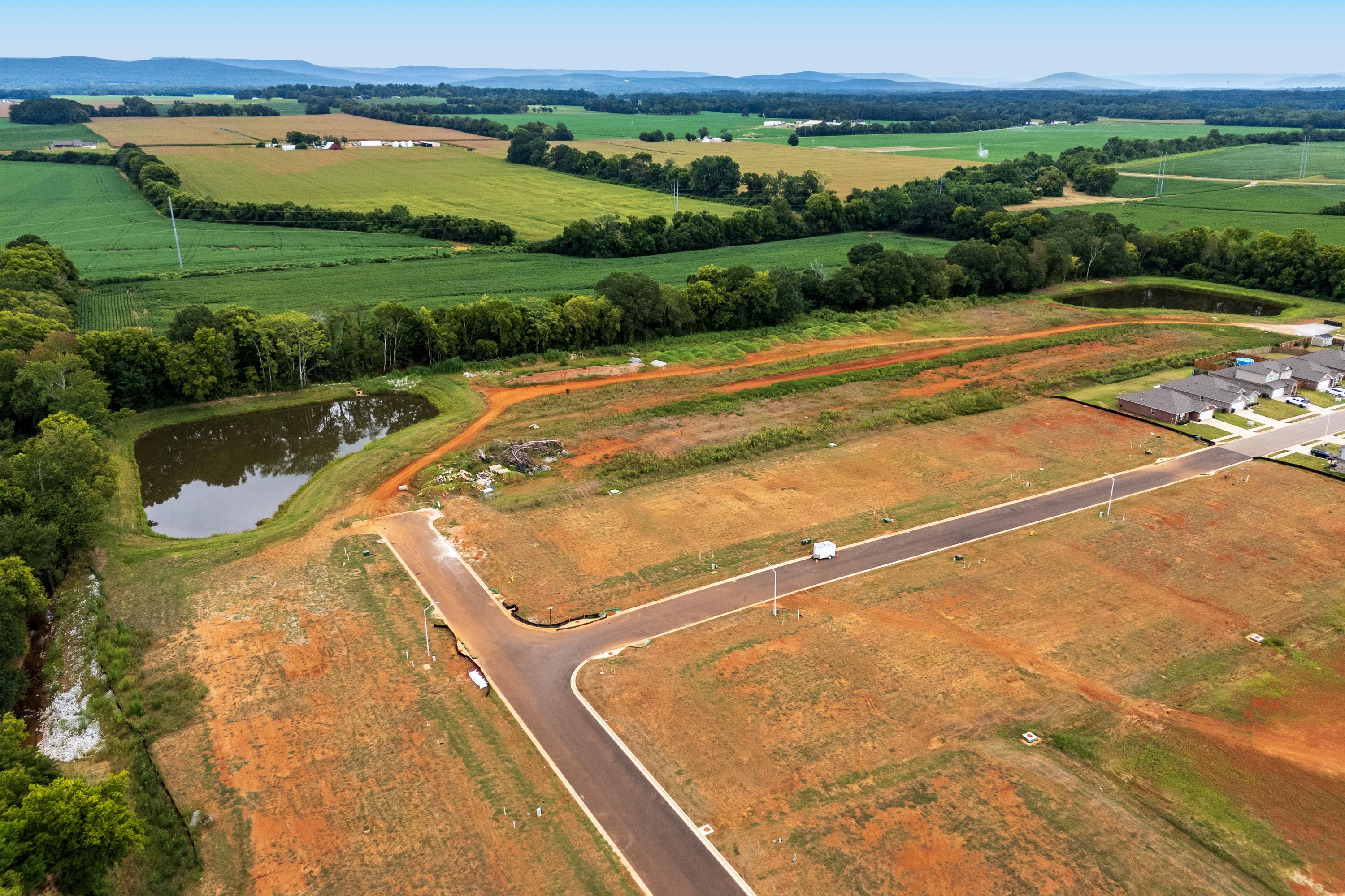 Aerial view of Lynn Meadows new home community in Meridianville AL with cleared lots, pond, and surrounding green fields