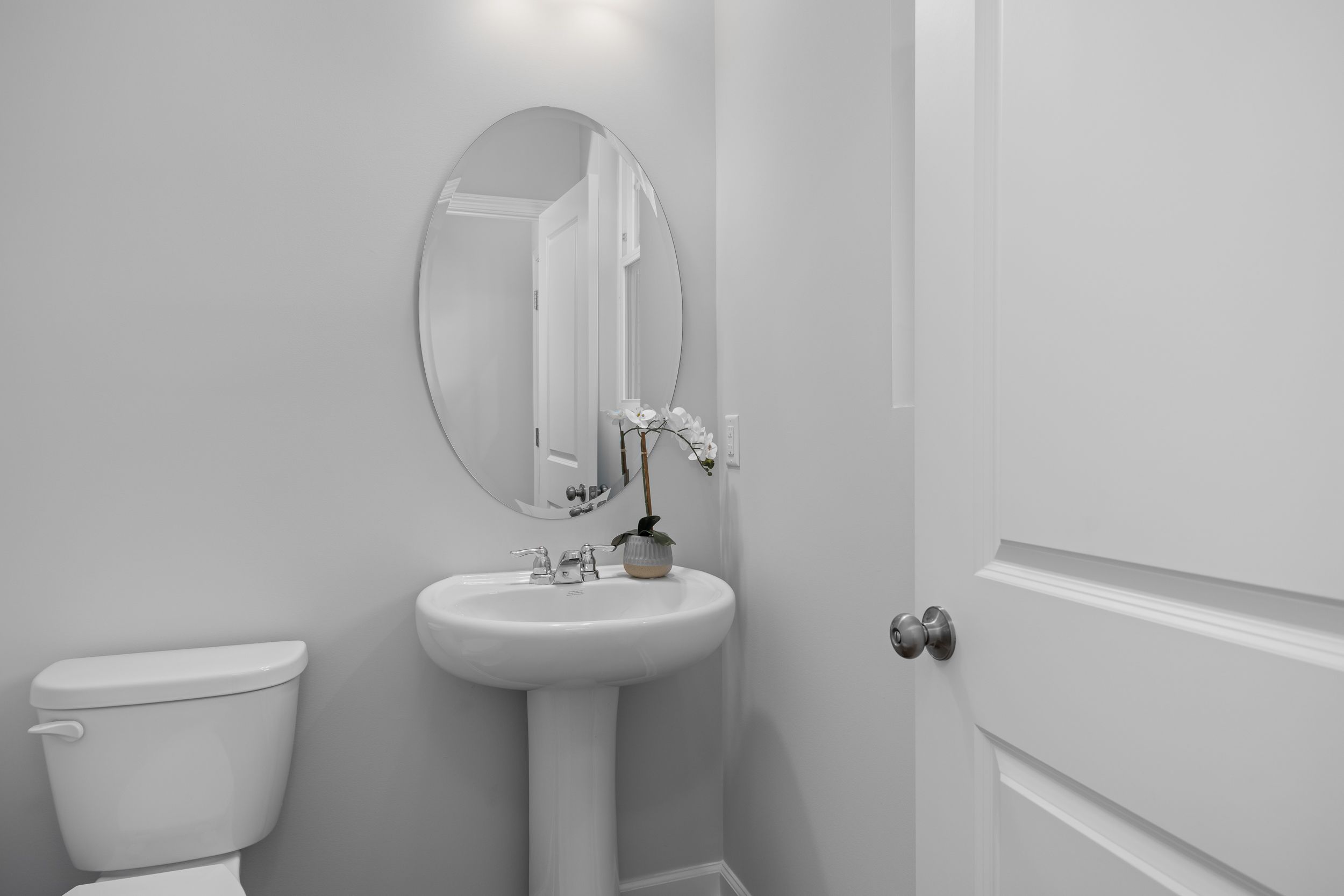 Modern powder room in The Warren featuring a classic pedestal sink, oval mirror, and sleek white interior finishes.