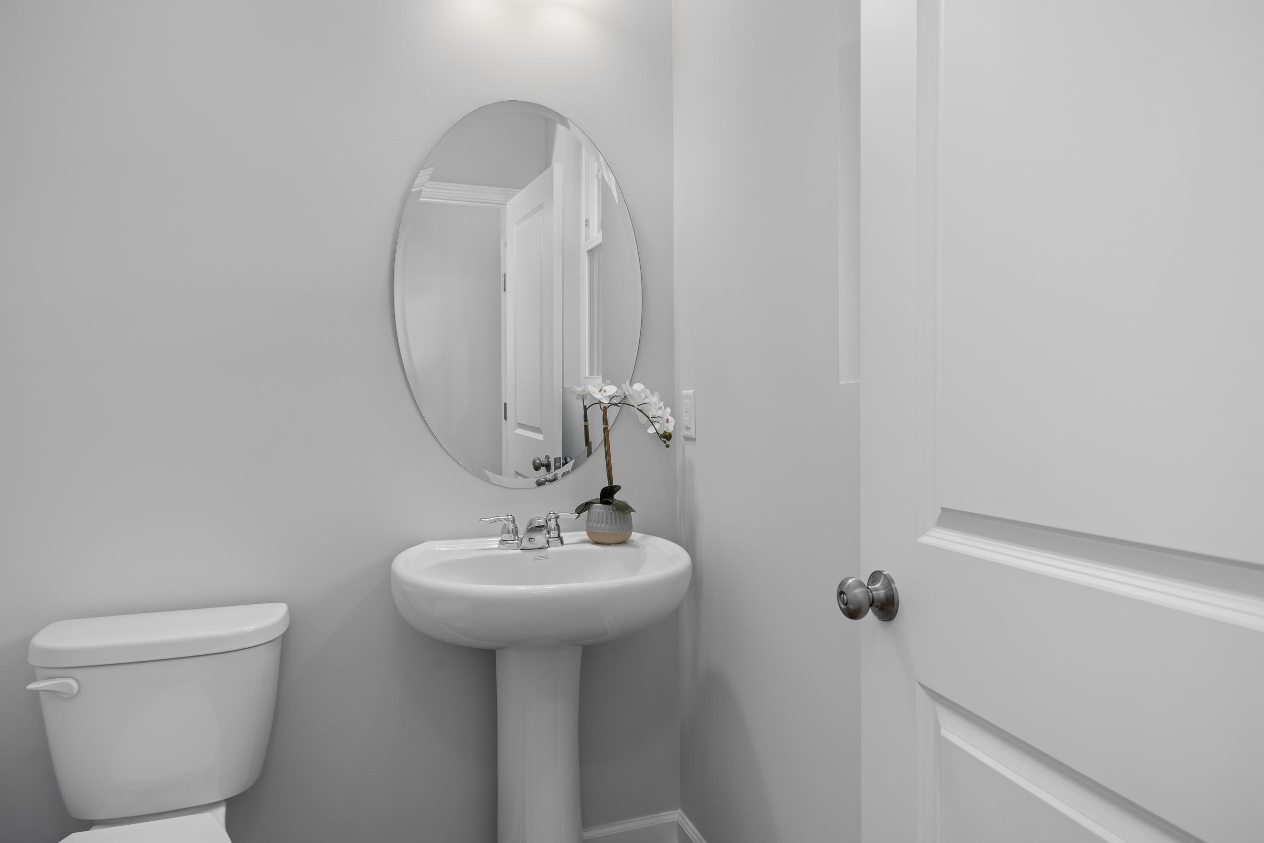 Modern powder room in The Warren featuring a classic pedestal sink, oval mirror, and sleek white interior finishes.