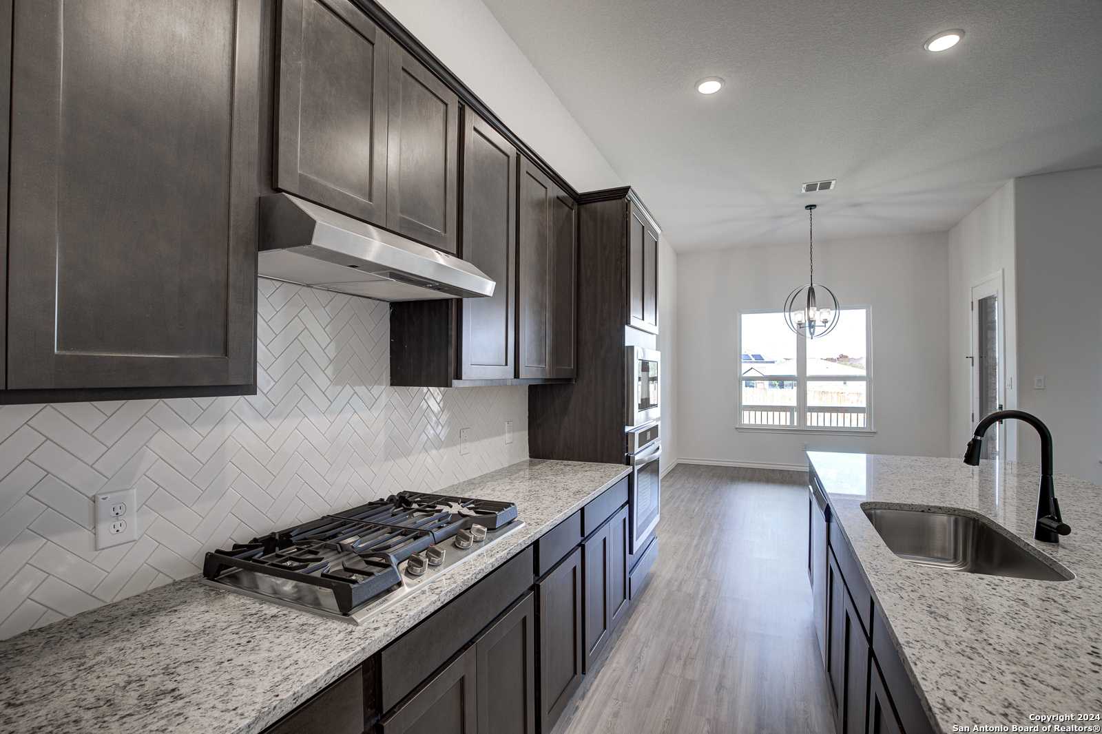 Modern kitchen with dark cabinets, herringbone tile backsplash, quartz counters, stainless appliances in The Garner B, Castroville, TX