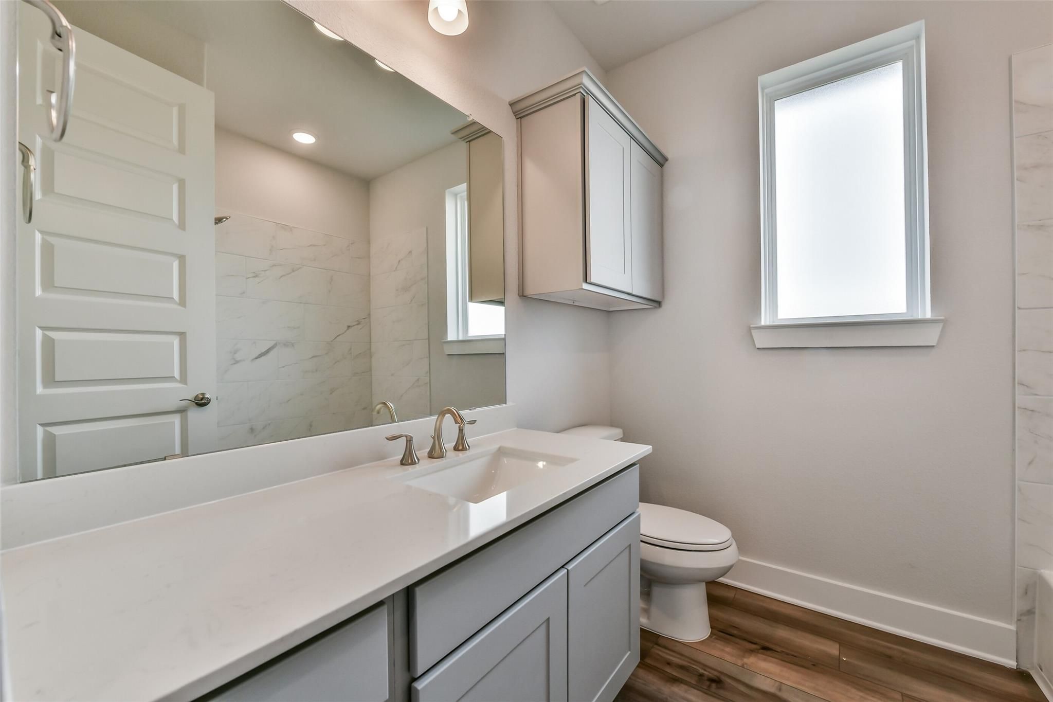 Modern bathroom with quartz double vanity, gray cabinets, marble walls, and window in Davidson Homes The George A, Lago Mar, Texas City