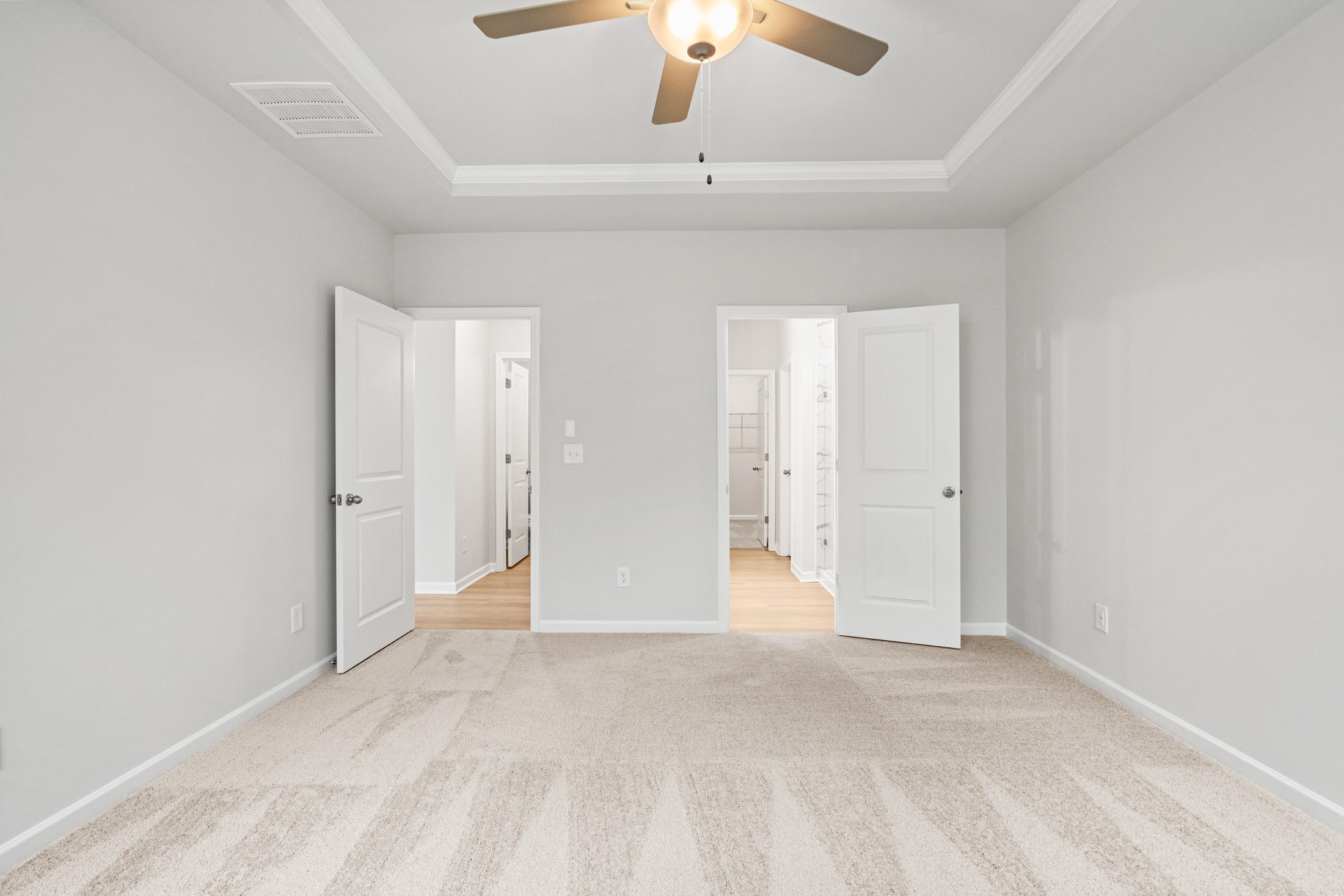 Spacious master suite in The Ash B at Wehunt Meadows with gray walls, ceiling fan, open bathroom and closet doors