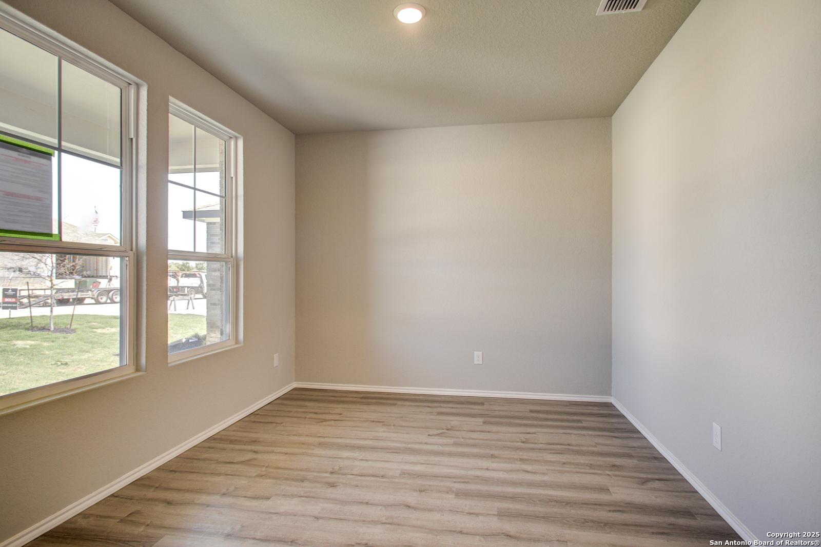 Bright empty living room with large windows, beige walls, and luxury vinyl plank floors in Davidson Homes The Douglas G, San Antonio