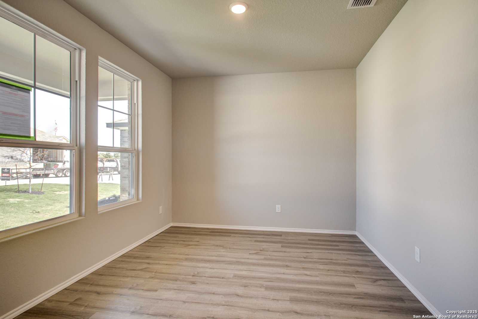 Bright empty living room with large windows, beige walls, and luxury vinyl plank floors in Davidson Homes The Douglas G, San Antonio