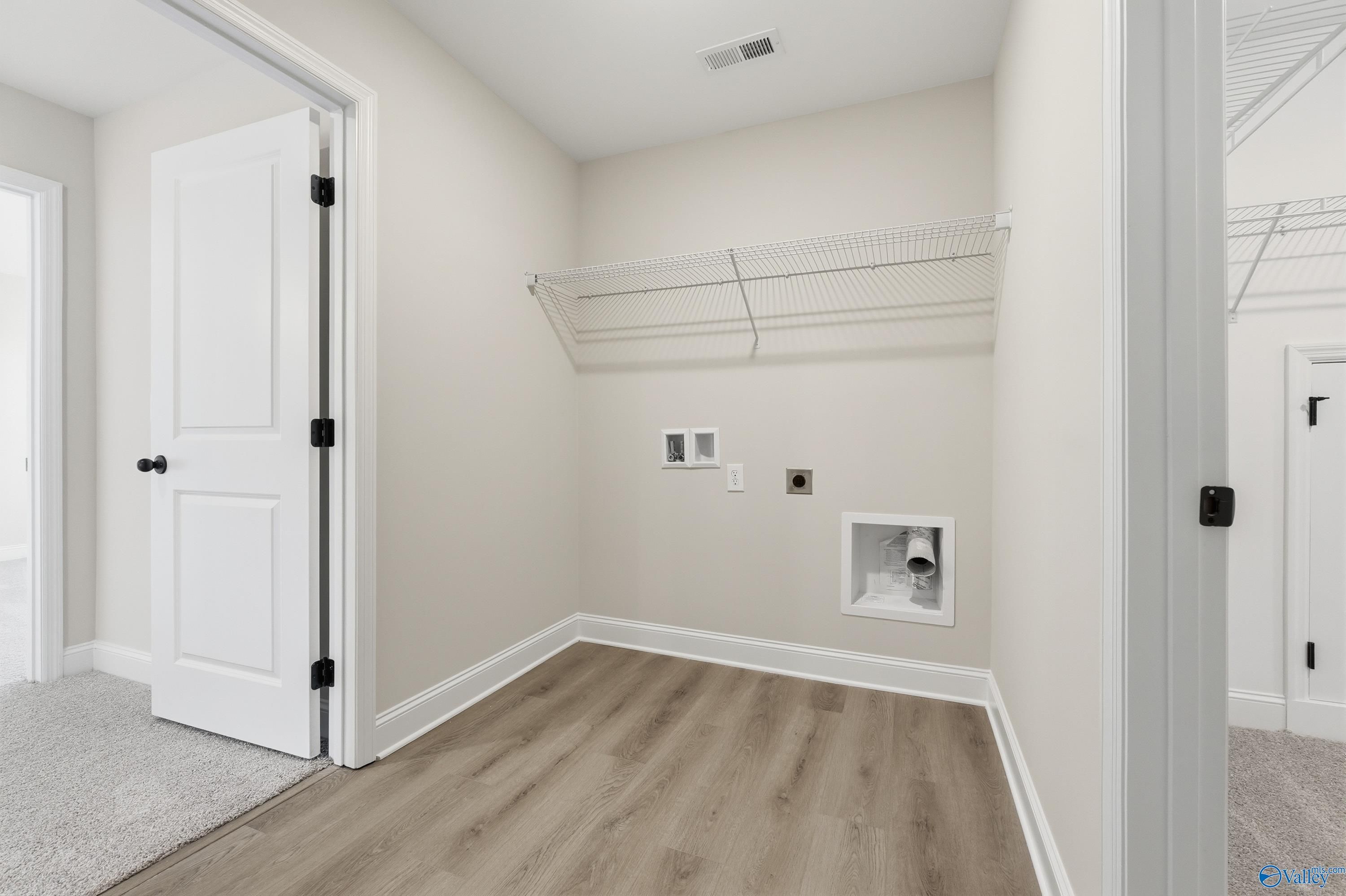 Spacious laundry room with wire shelving, utility hookups, and hardwood floors in Davidson Homes The Chelsea C, Harvest AL