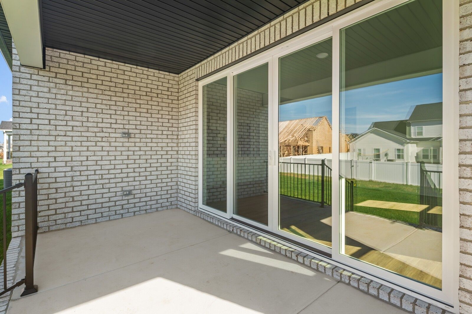 Covered patio with large sliding glass doors, brick walls, and black railing overlooking grassy yard in Davidson Homes The Hawkins, Murfreesboro