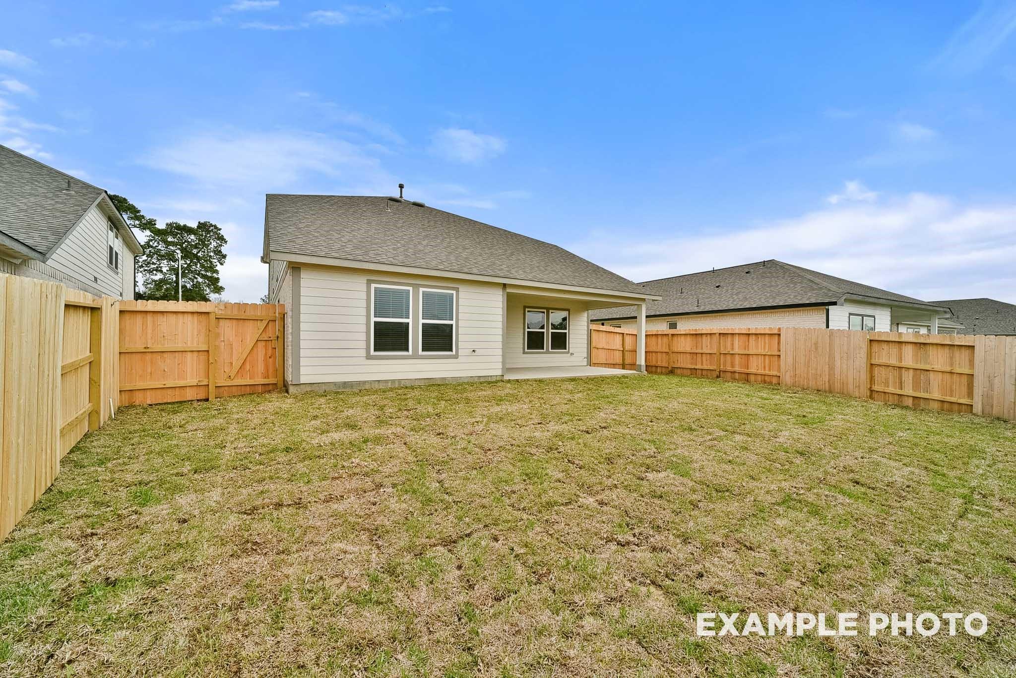 Backyard of 4-bedroom Tierra B home featuring covered patio, wood fence, and lush lawn in Emberly, Beasley, Texas