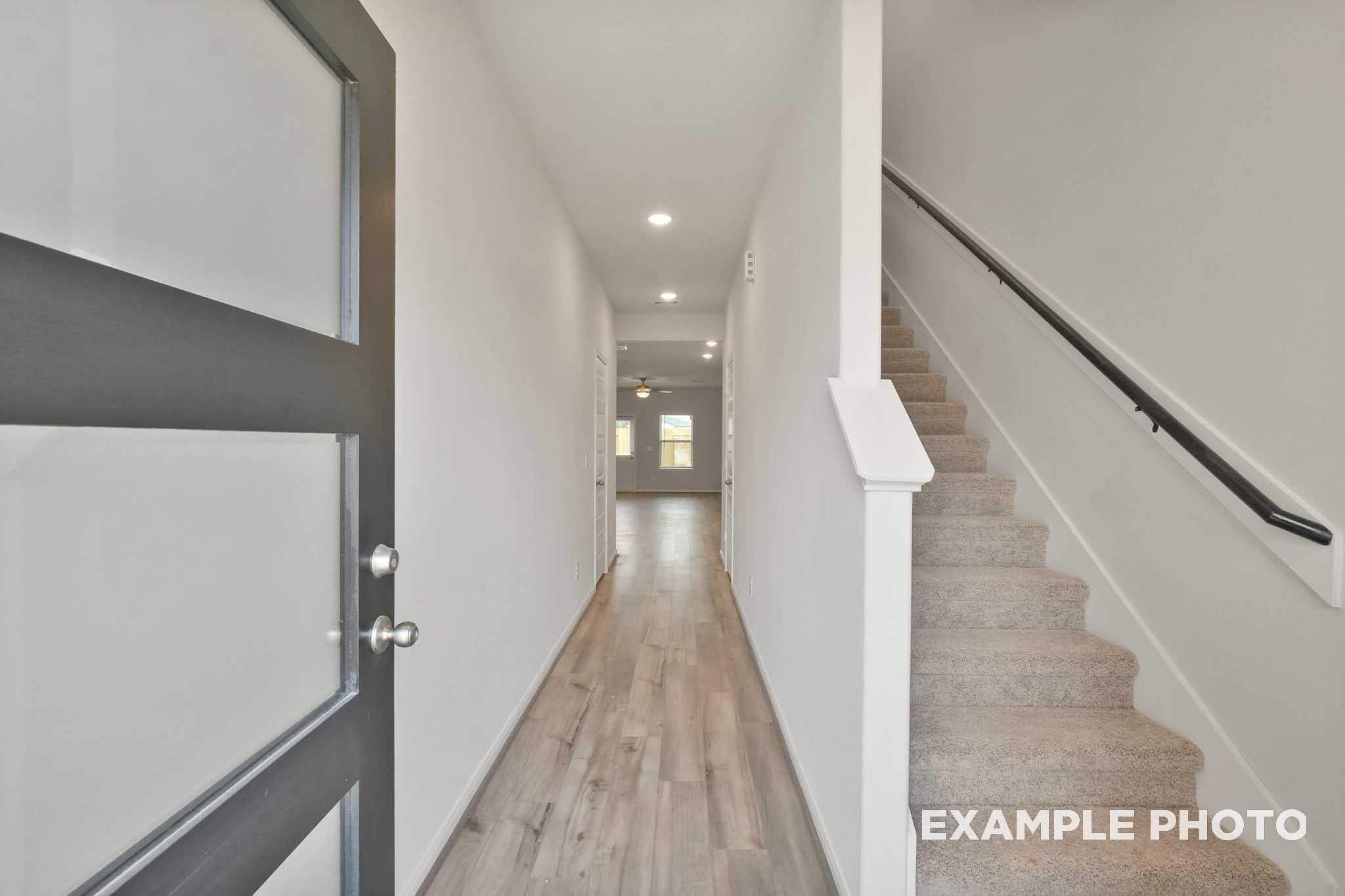 Bright entry foyer with wood-look flooring, frosted glass front door, and carpeted staircase in Davidson Homes Brazos E, Conroe TX