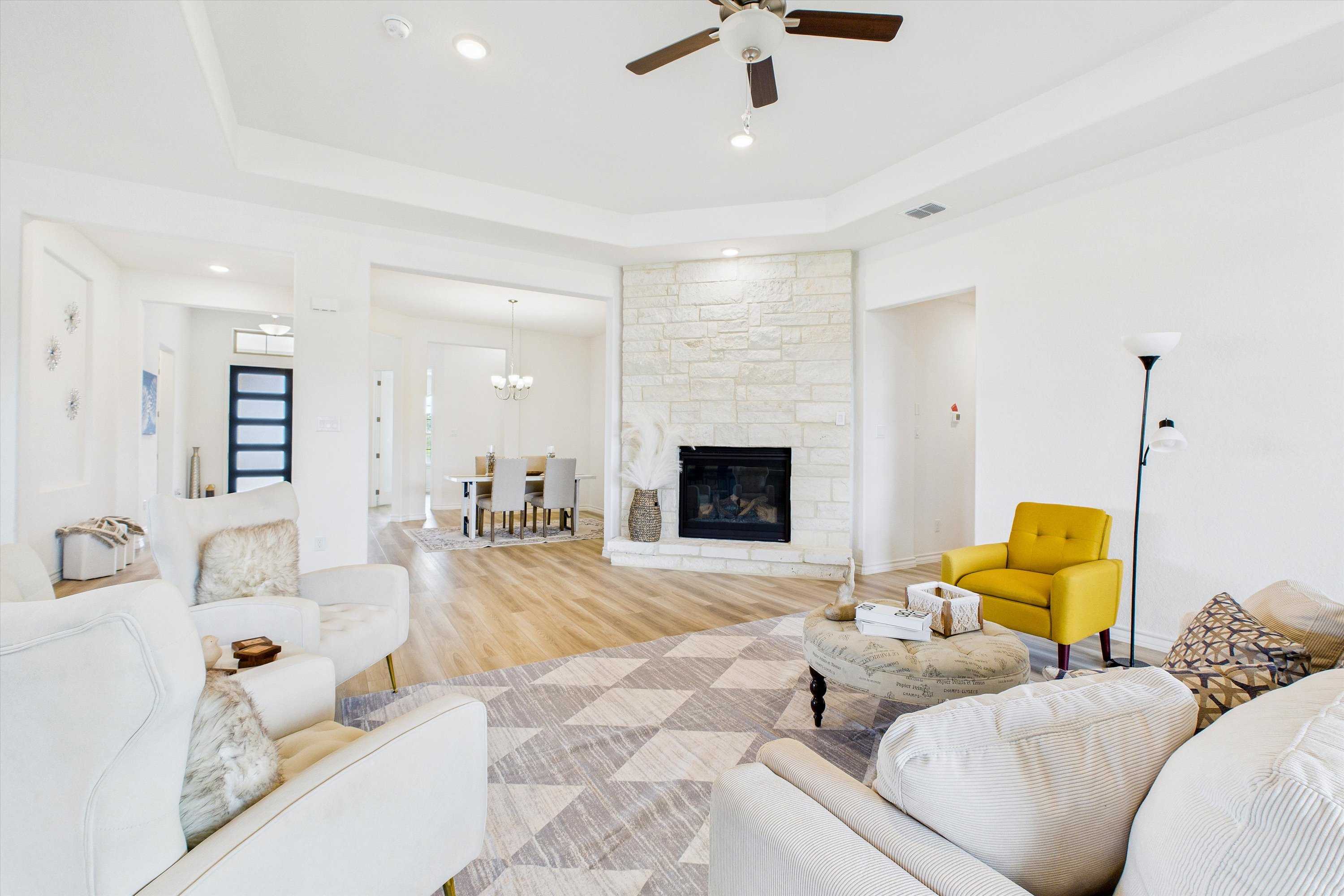 Open-concept living room with stone fireplace, white sofas, yellow accent chair, and dining nook in Davidson Homes The Summerlin C, Castroville, Texas