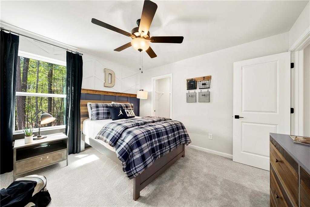 Boy's bedroom with plaid bedding, wooden headboard, ceiling fan, and wooded view window in Davidson Homes The Hickory B, Dallas, Georgia