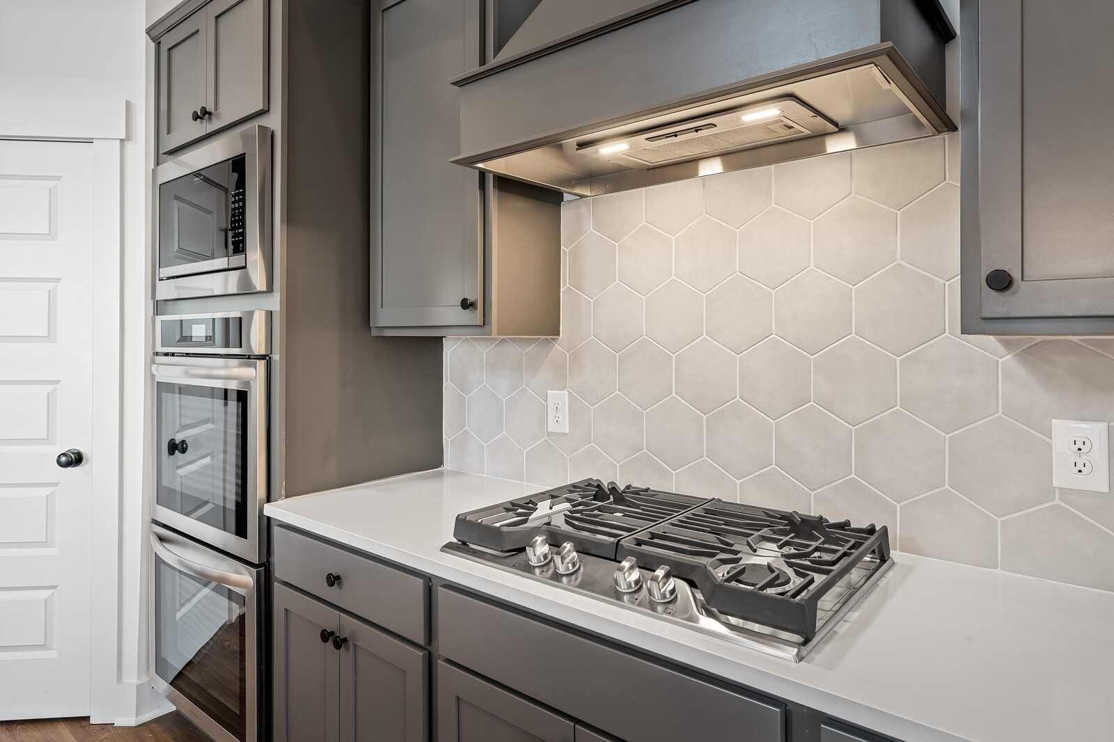 Modern kitchen featuring gray shaker cabinets, white quartz counters, gas cooktop, double ovens, and geometric tile backsplash in Davidson Homes Ridgeport, Gallatin TN