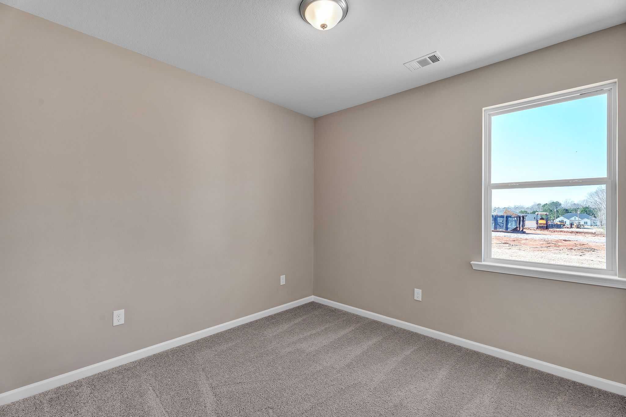 Spacious bedroom interior at Anderson Lakes in Opelika AL by Davidson Homes featuring beige walls, neutral carpet, and large window