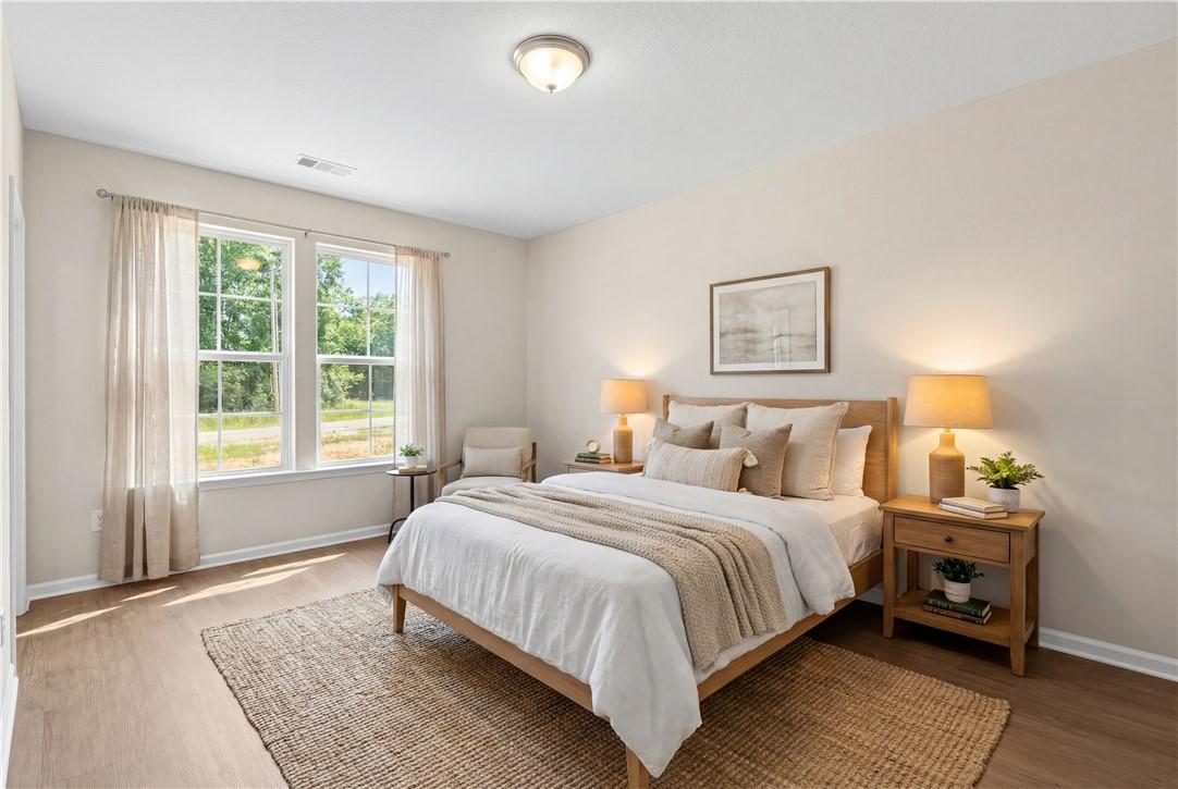 Bright master bedroom with king bed, neutral bedding, lamps, and garden views in Evermore Homes The Orion, Cusseta, Alabama