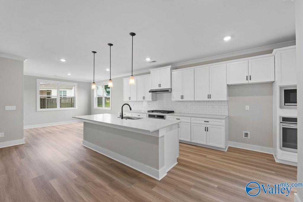 Modern white kitchen featuring large island, stainless steel appliances, subway tile backsplash in Evermore Homes The Oxford, Owens Cross Roads, AL