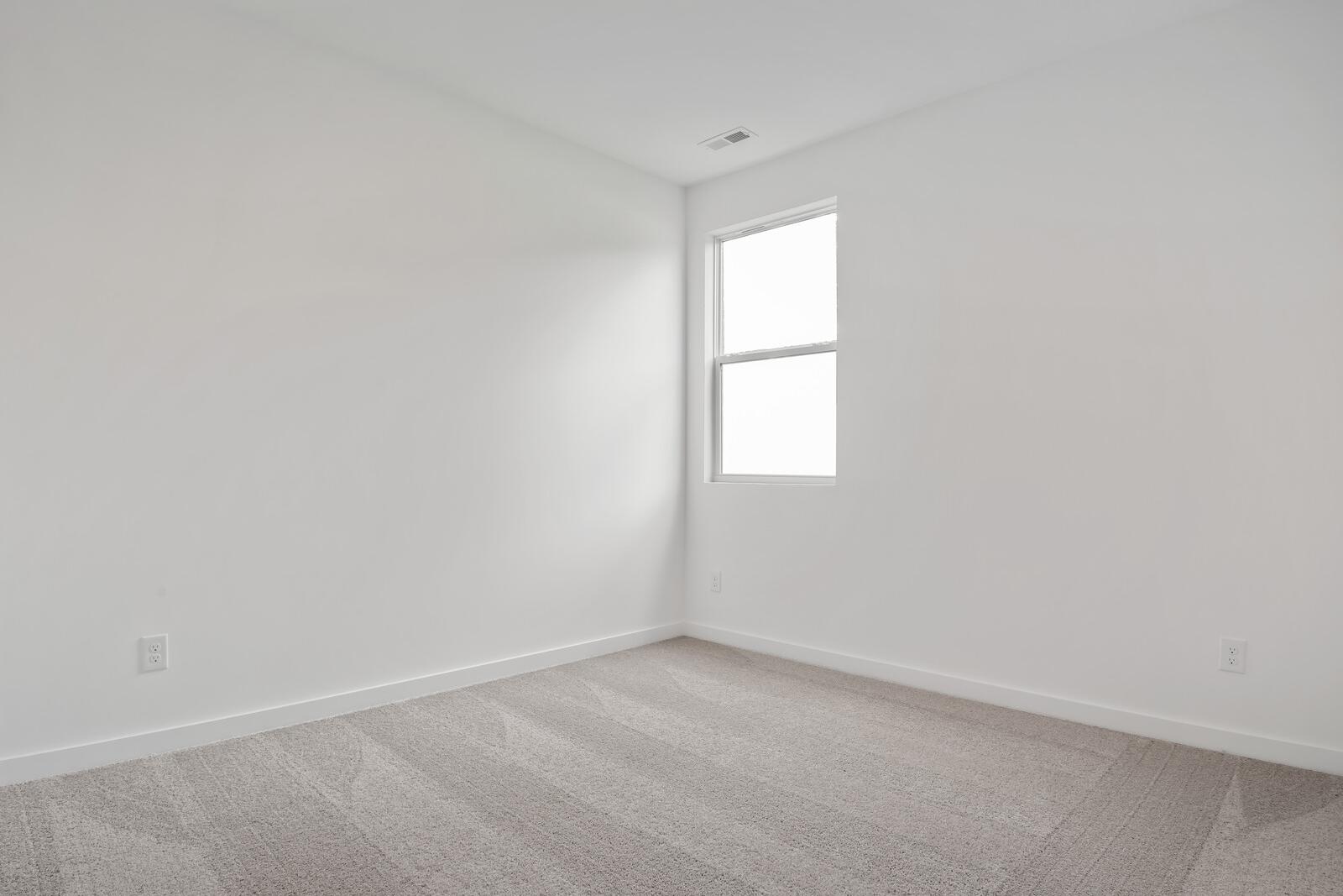 Spacious empty bedroom corner in The Asheville home with white walls, large window, beige carpet, and outlets
