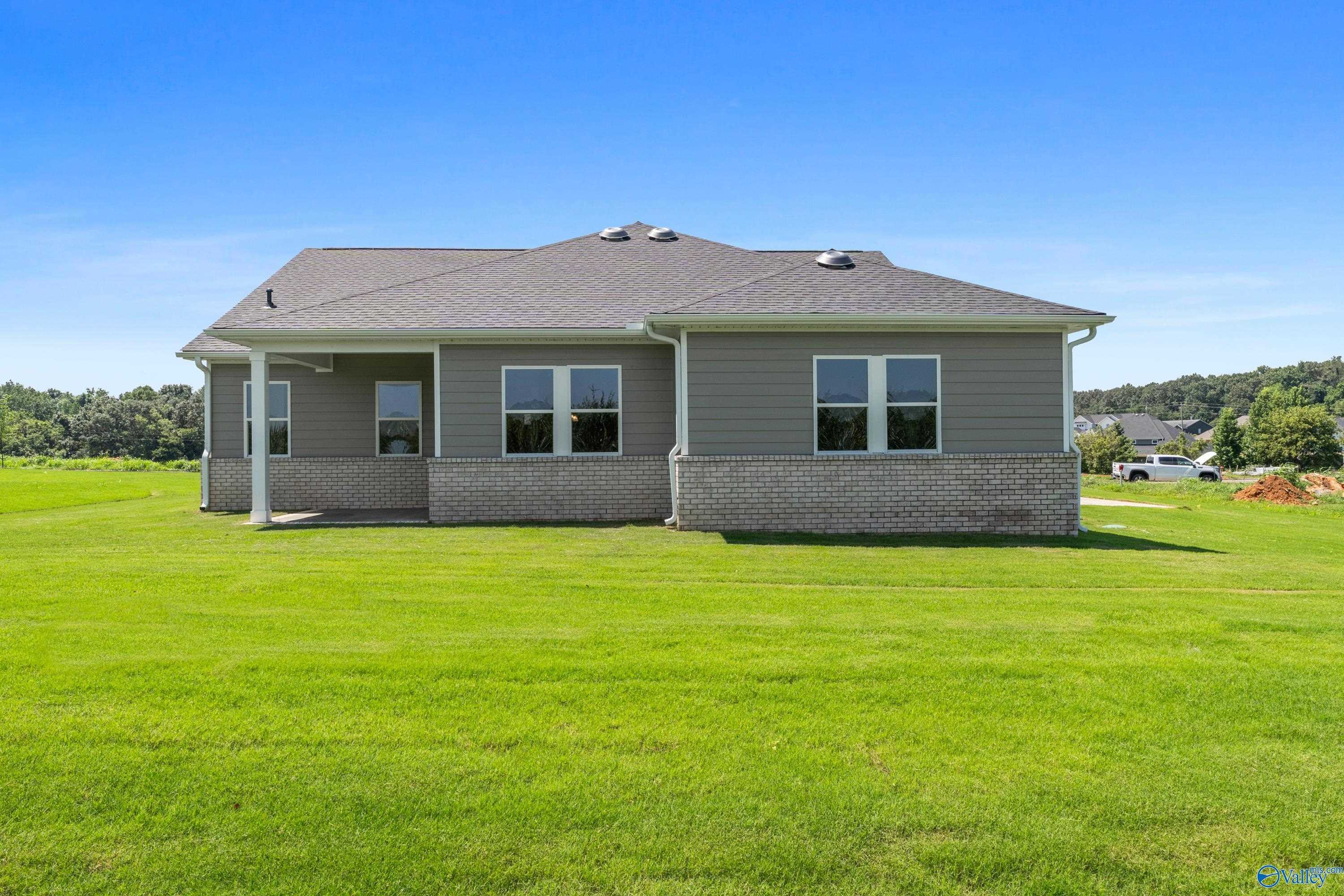 Rear view of single-story 4-bedroom Arcadia home with covered porch, gray siding, and lush green yard in Riverton Preserve, Huntsville, Alabama