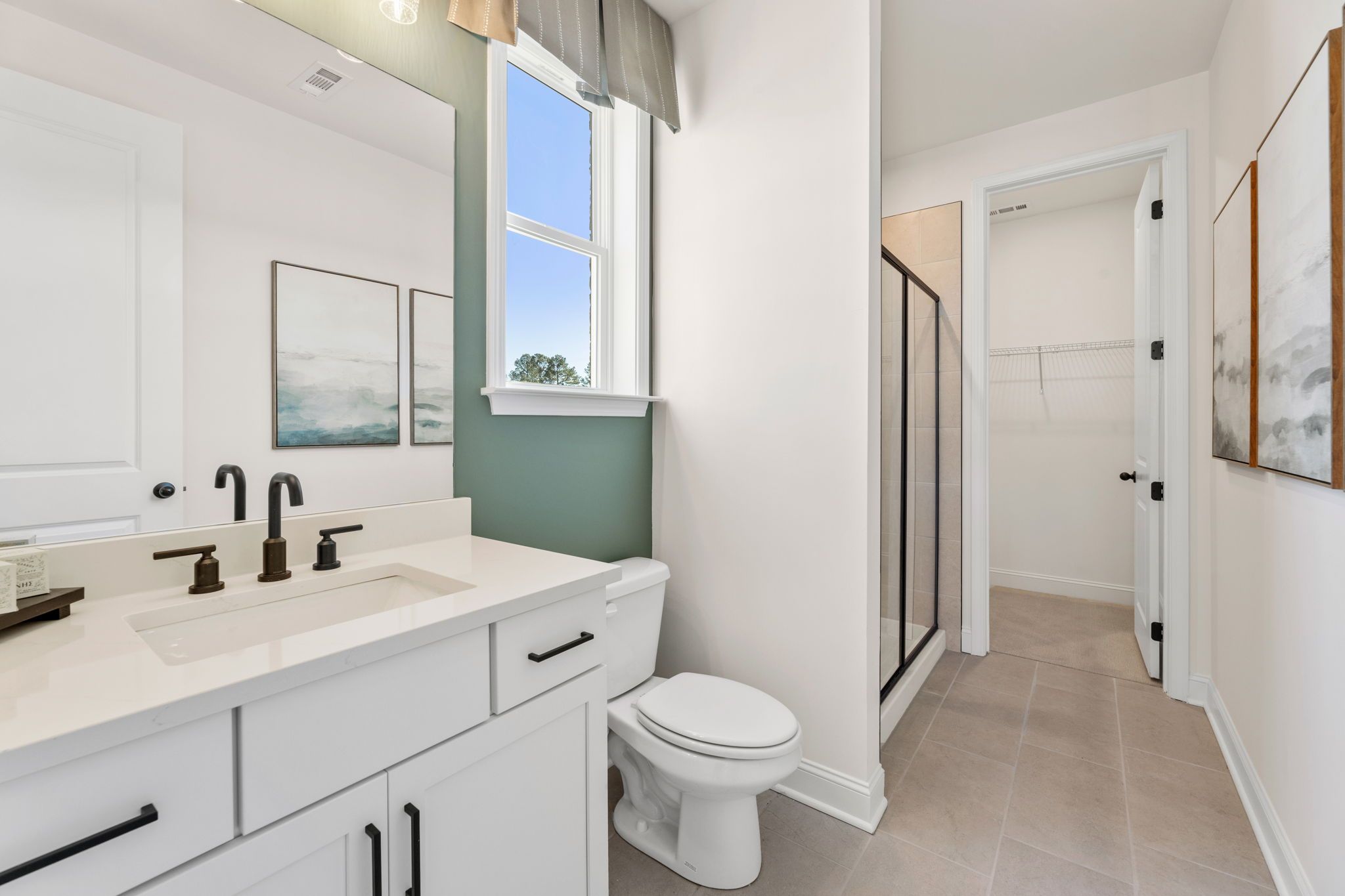 Modern bathroom in Fern Hollow Buford GA with white vanity black faucets glass shower green accent wall by Davidson Homes