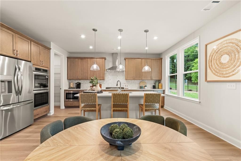 Open-concept kitchen with wood cabinetry, stainless appliances, island seating, and dining area in Davidson Homes Danbury E, Buford GA