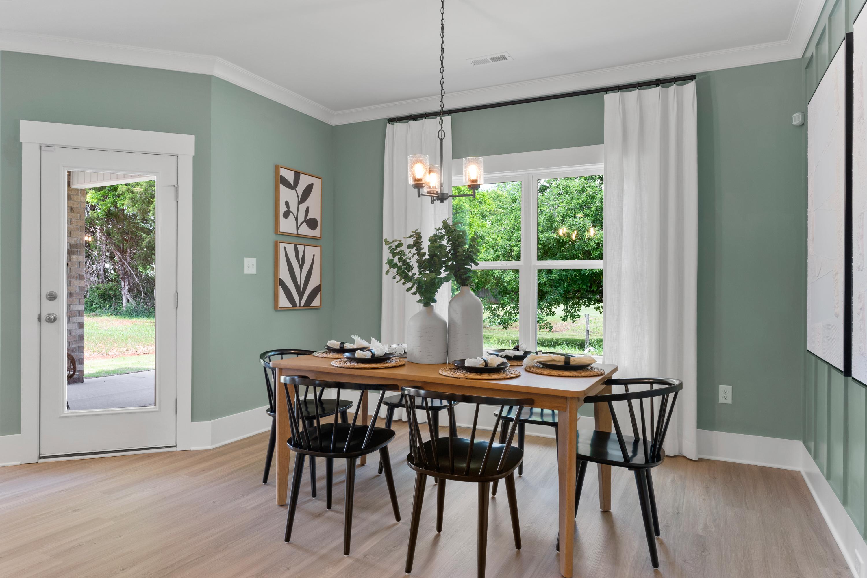Elegant dining room in Hollon Meadow Decatur AL with wooden farmhouse table, sage green walls, chandelier, and garden view windows