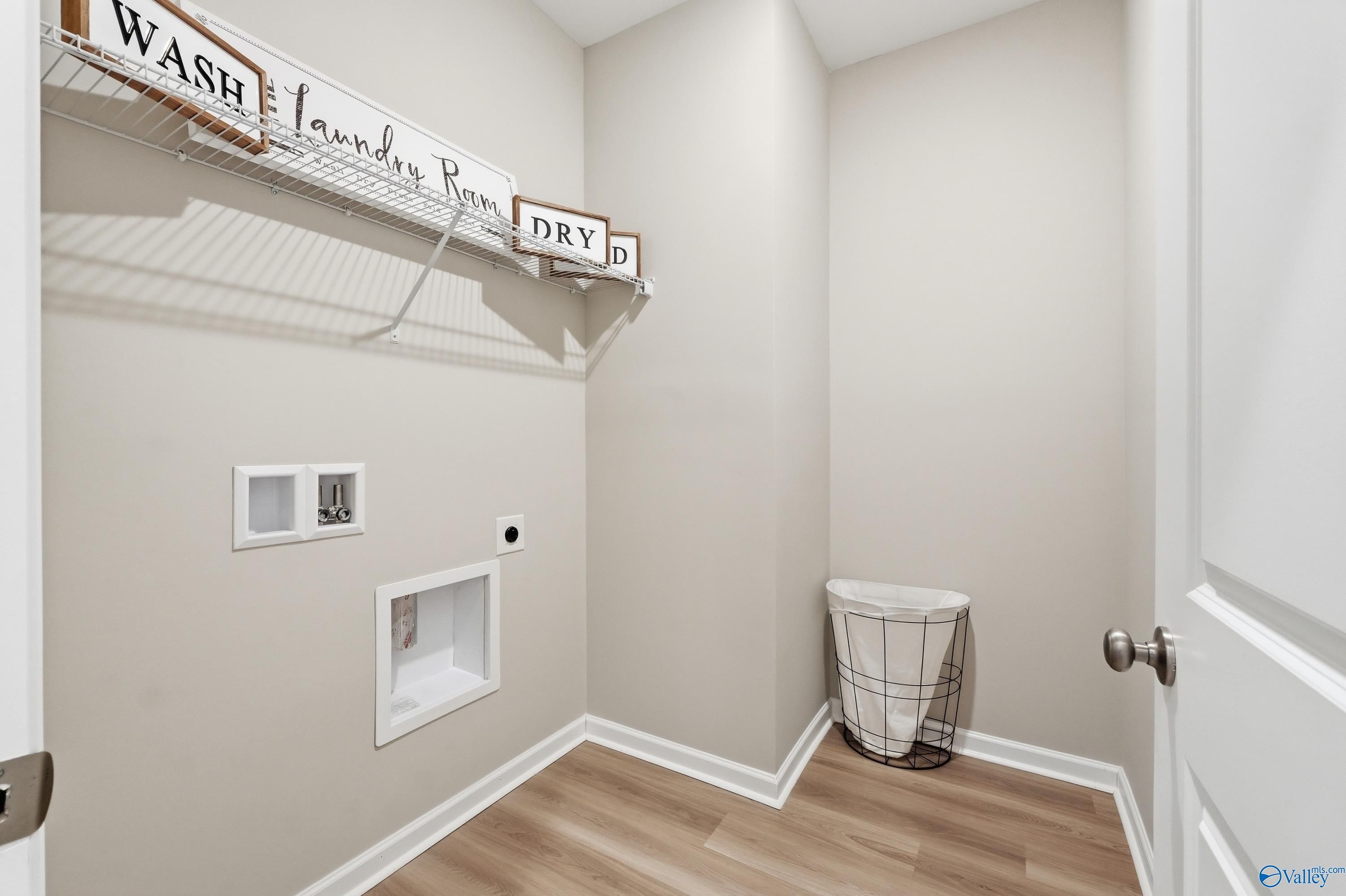 Functional laundry room with washer-dryer hookups, wooden "Wash Laundry Room" sign, and beige walls in Davidson Homes The Polaris, Fayetteville, TN