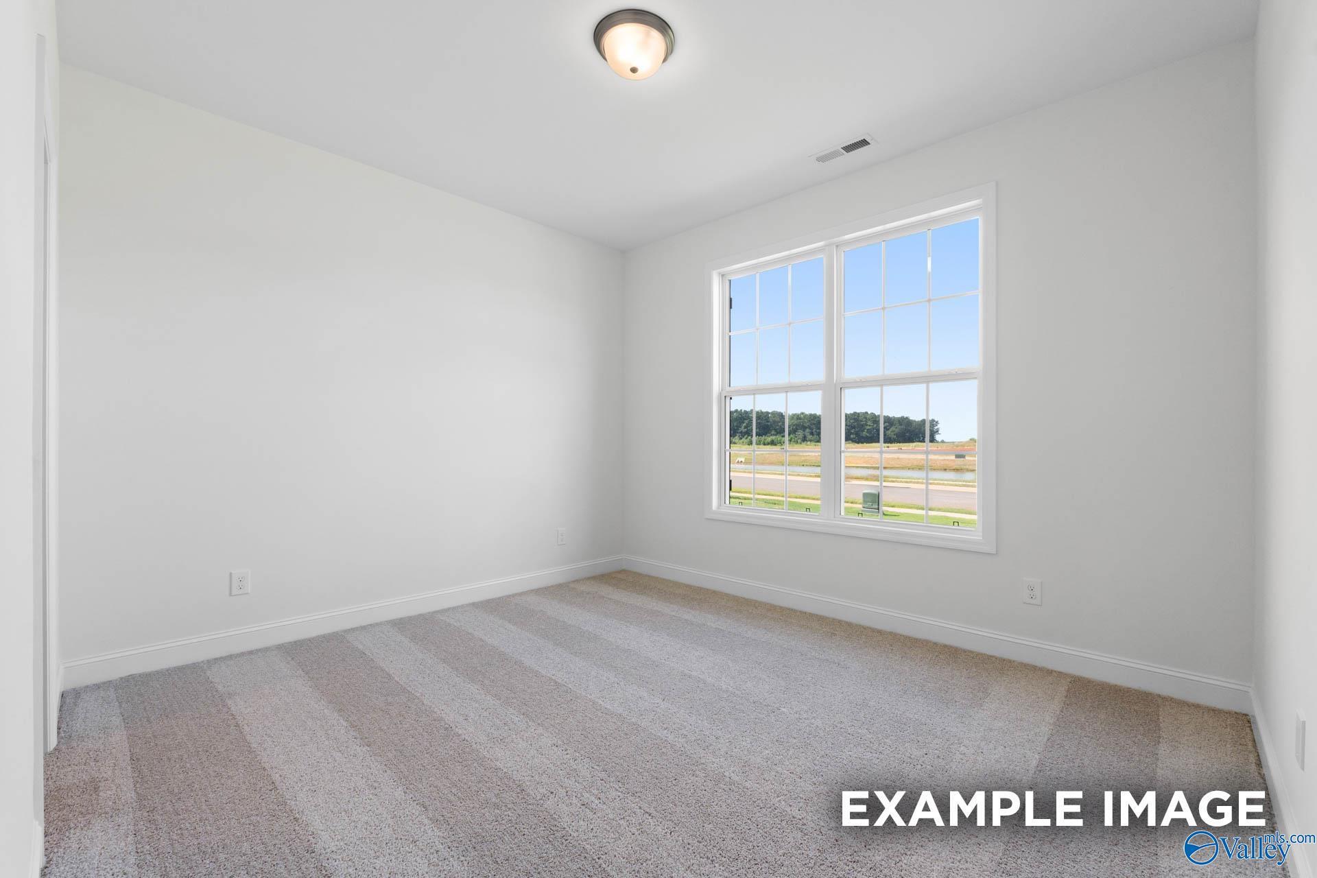 Bright, carpeted bedroom with large window in The Rockford B floor plan at Kendall Downs, Toney, Alabama.