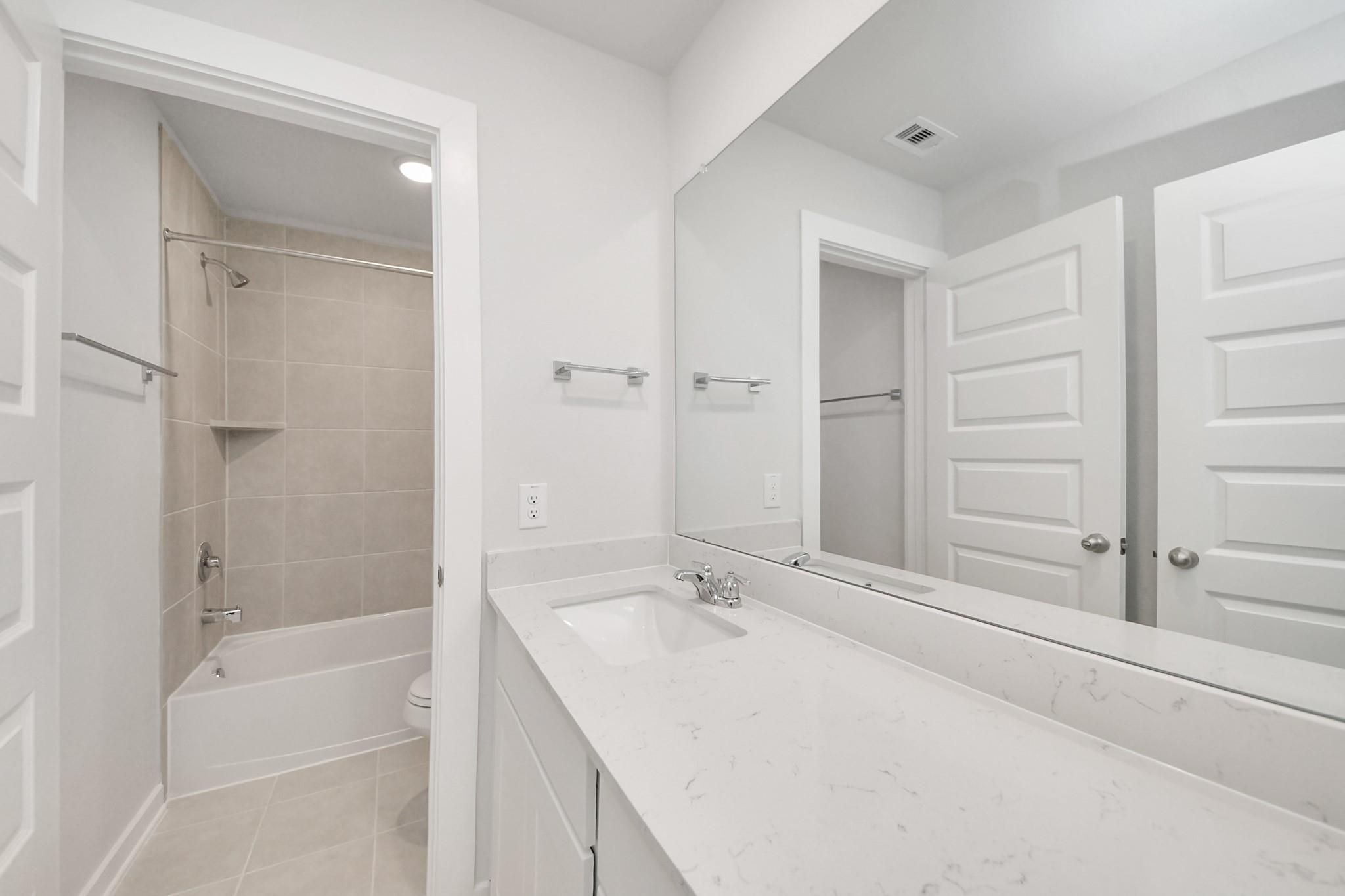 Modern bathroom with white vanity, quartz countertop, and tub-shower combo in The Blanco E at Caney Creek Place, Conroe.