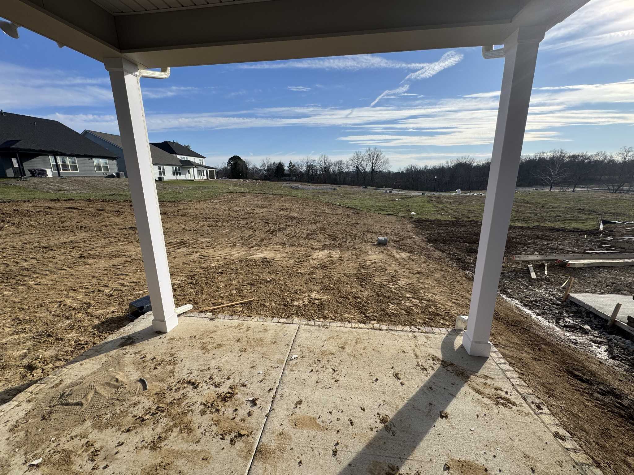 Covered porch with white columns and concrete patio overlooking graded backyard in Davidson Homes The Ridgeport, Woods Crossing, Gallatin, Tennessee