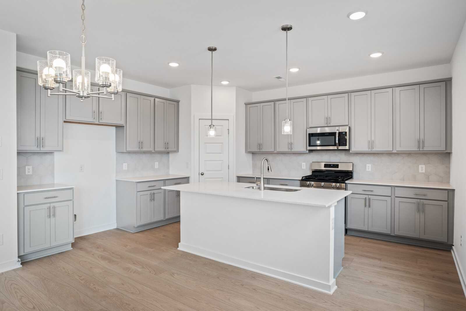 Modern gray cabinet kitchen with white quartz island, stainless steel appliances, pendant lights in Davidson Homes The Logan B, White House, TN