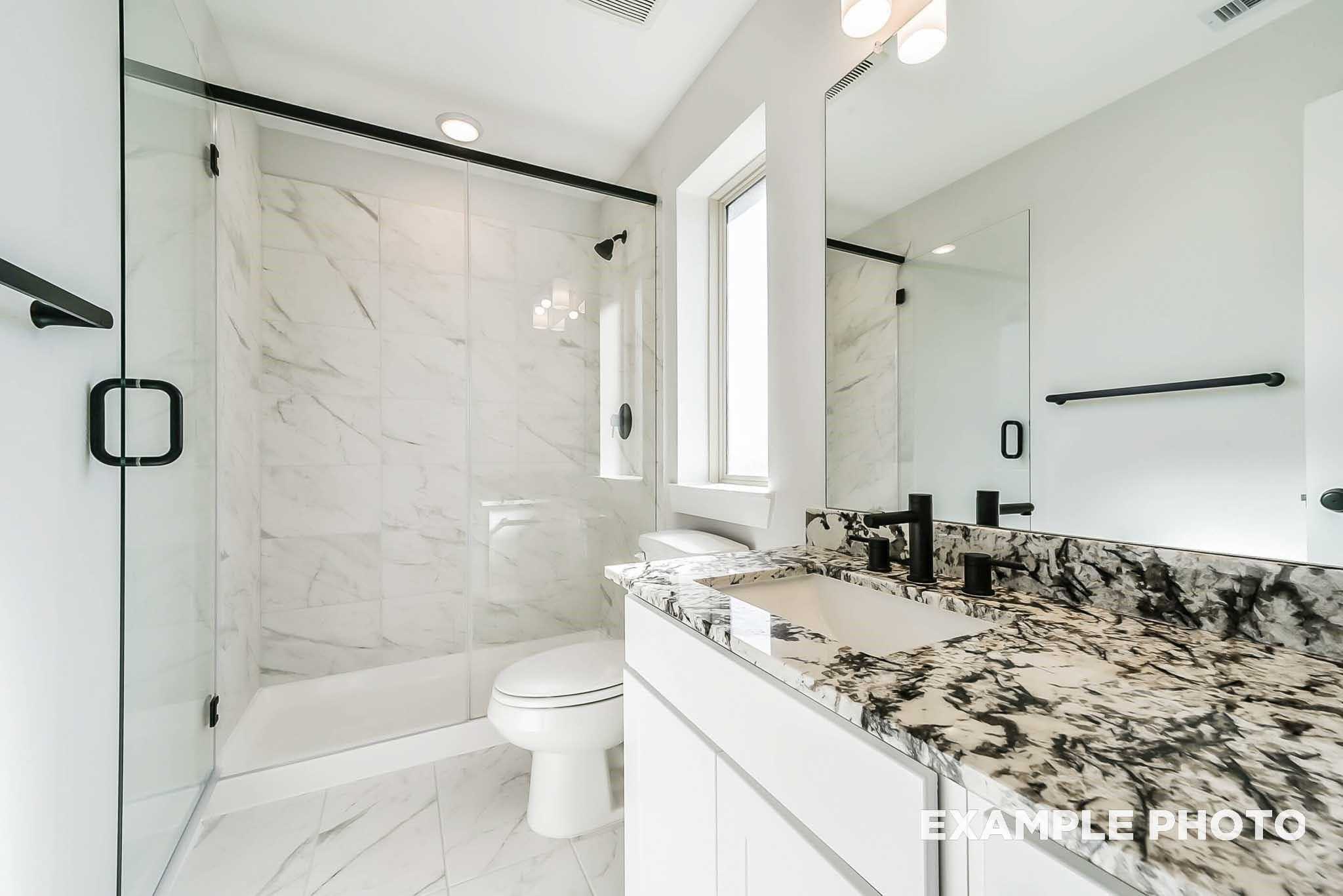 Modern bathroom featuring frameless glass shower, marble-look walls, granite vanity, and large mirror in Davidson Homes The Philip C, Rosharon, Texas
