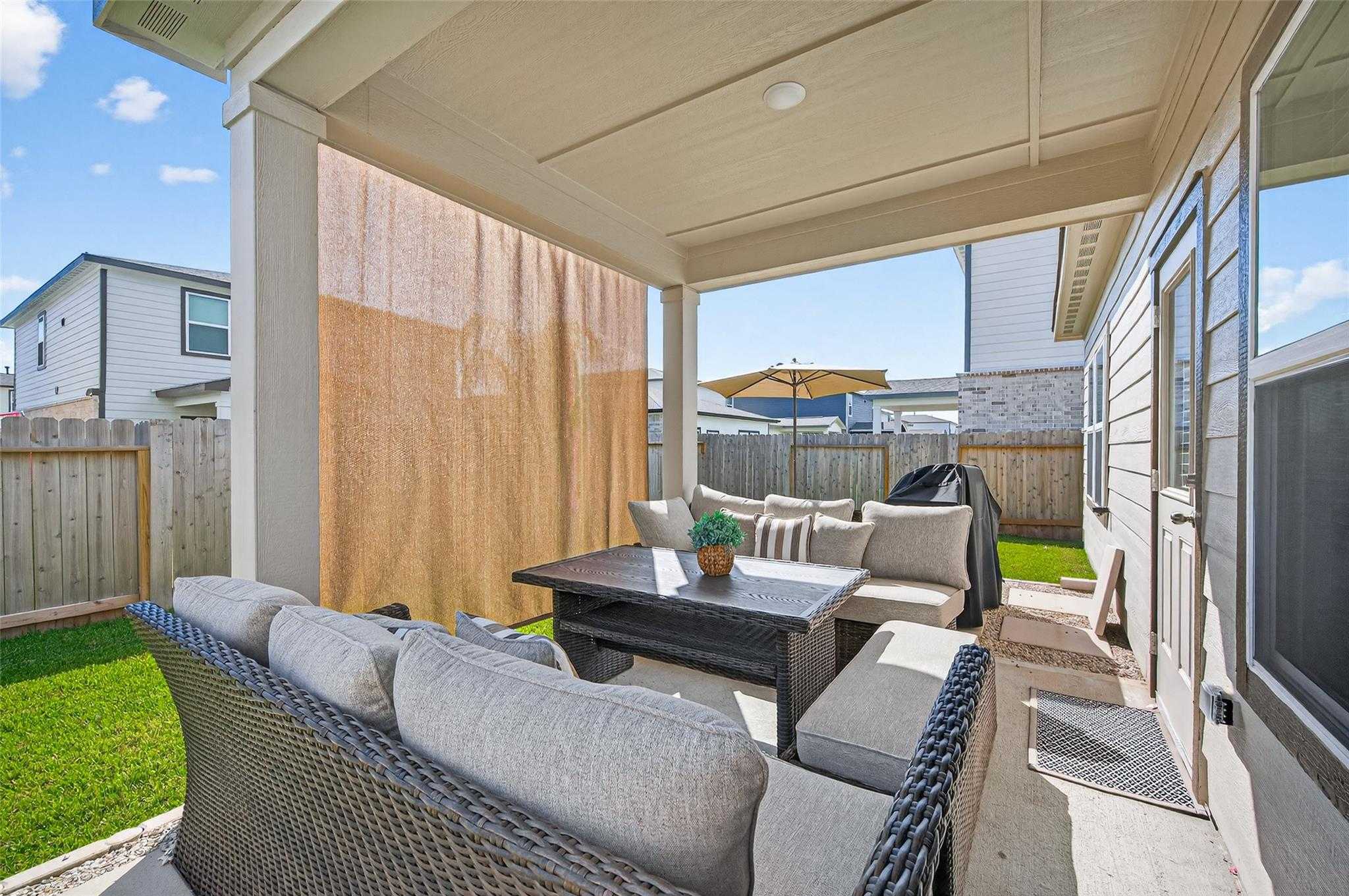 Inviting covered back patio with beige sectional sofa, coffee table, grill, and privacy screens in Davidson Homes The Brazos E, Magnolia, Texas