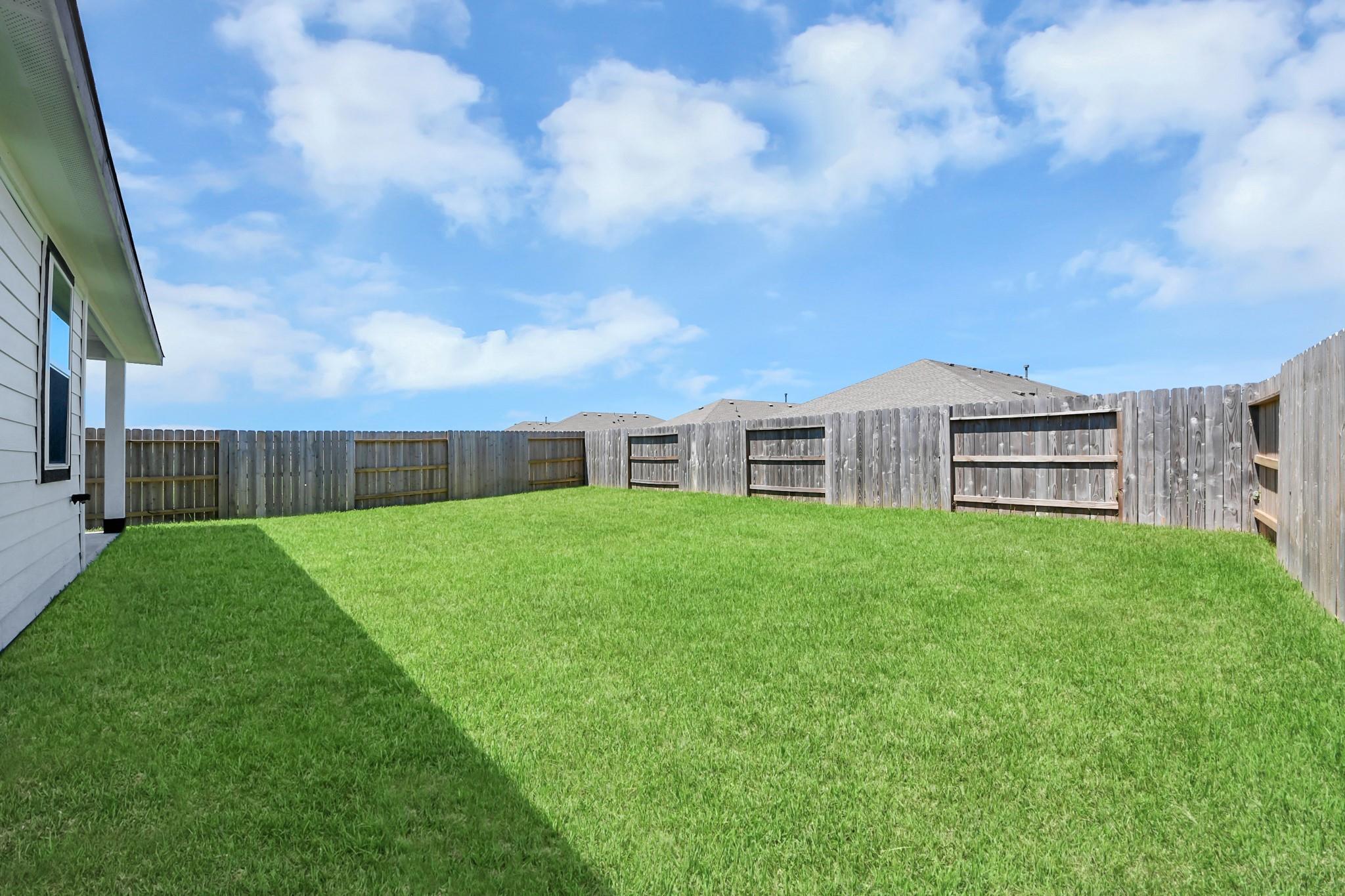 Spacious fenced backyard with lush green lawn at Davidson Homes The Costa A in Emberly, Beasley, Texas