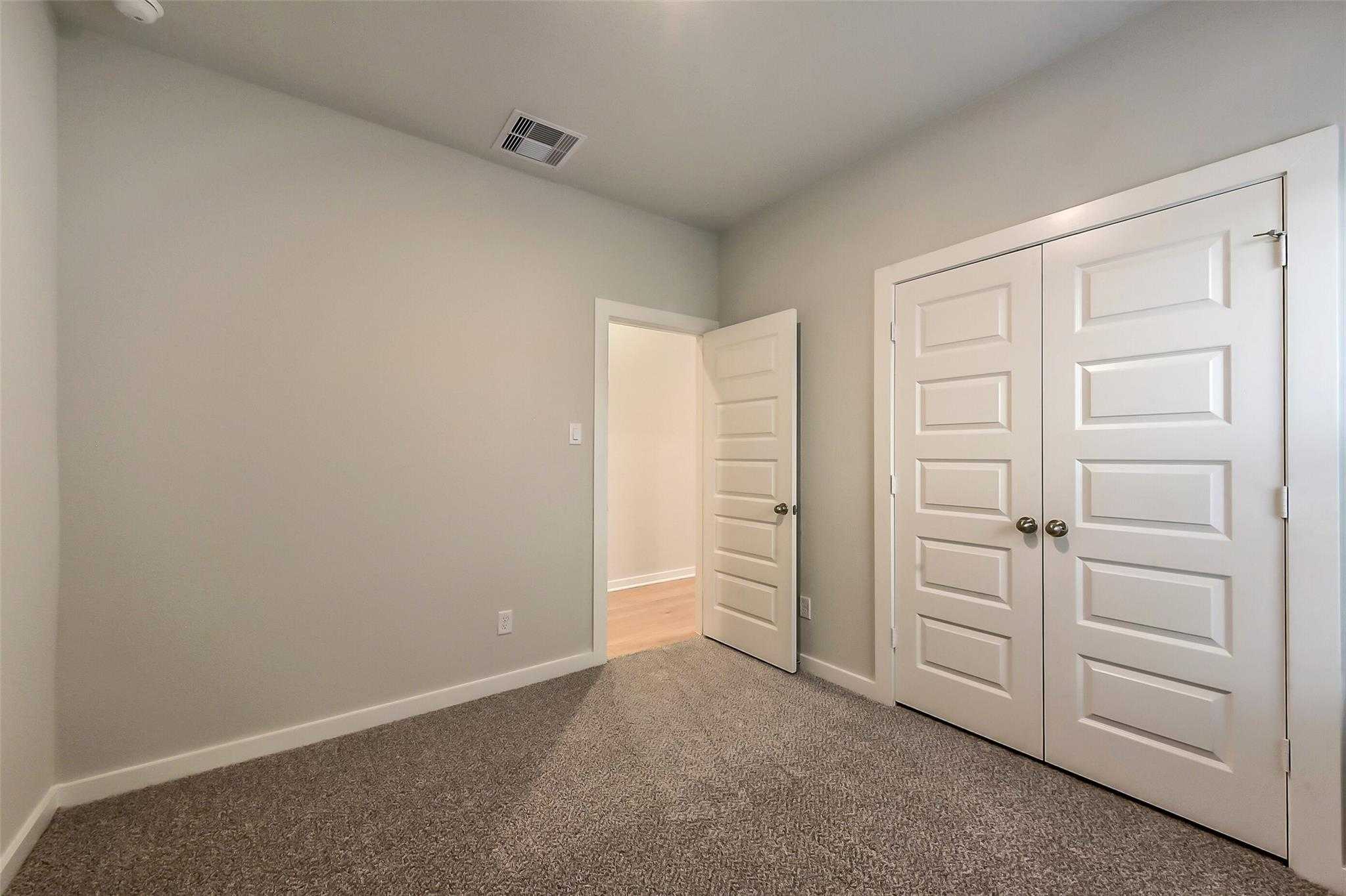 Bright master bedroom with neutral gray walls, carpet floor, double closet doors, and open en-suite in Davidson Homes The Laguna B, Katy, TX