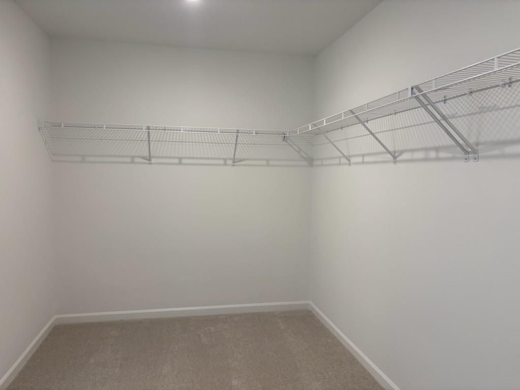 Spacious walk-in closet with white wire shelving and beige carpet in The Hickory B, Davidson Homes, Cedar Farms, Winder, Georgia