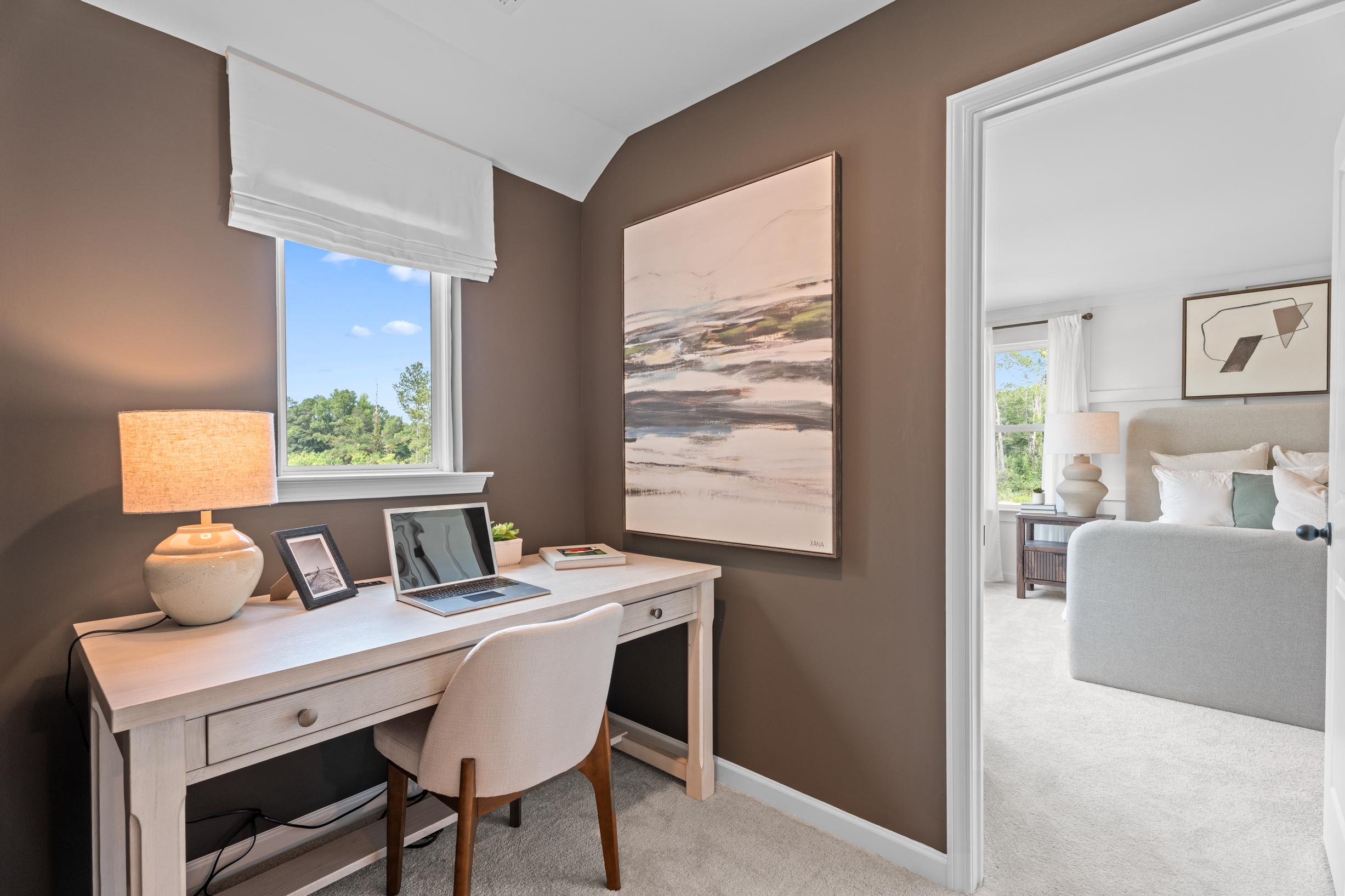 Home office with desk and laptop at Links Crossing in Auburn, Alabama by Davidson Homes, featuring a view into the bedroom.