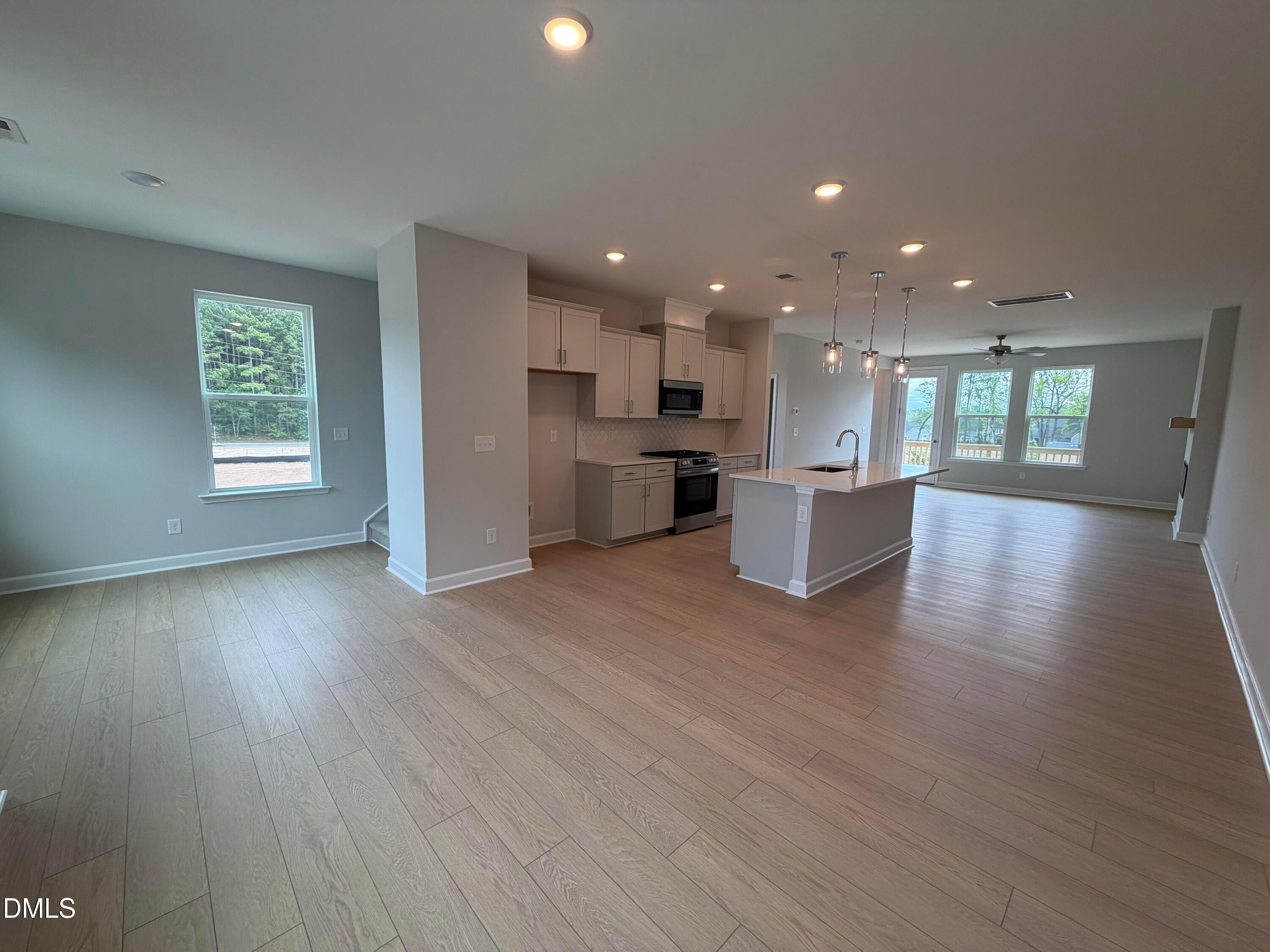 Modern open-concept kitchen with white cabinets, stainless appliances, large island, and hardwood floors in The Mitchell 4-bedroom home, Knightdale, NC