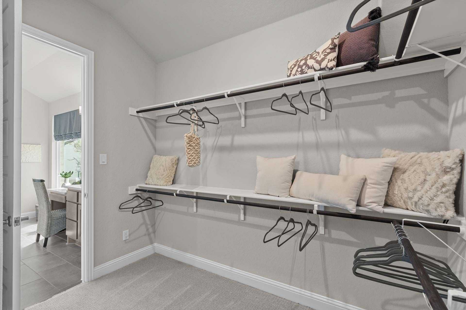 Spacious walk-in closet in Ladera San Antonio home by Davidson Homes with white shelving, hanging rods, pillows, and adjacent office nook