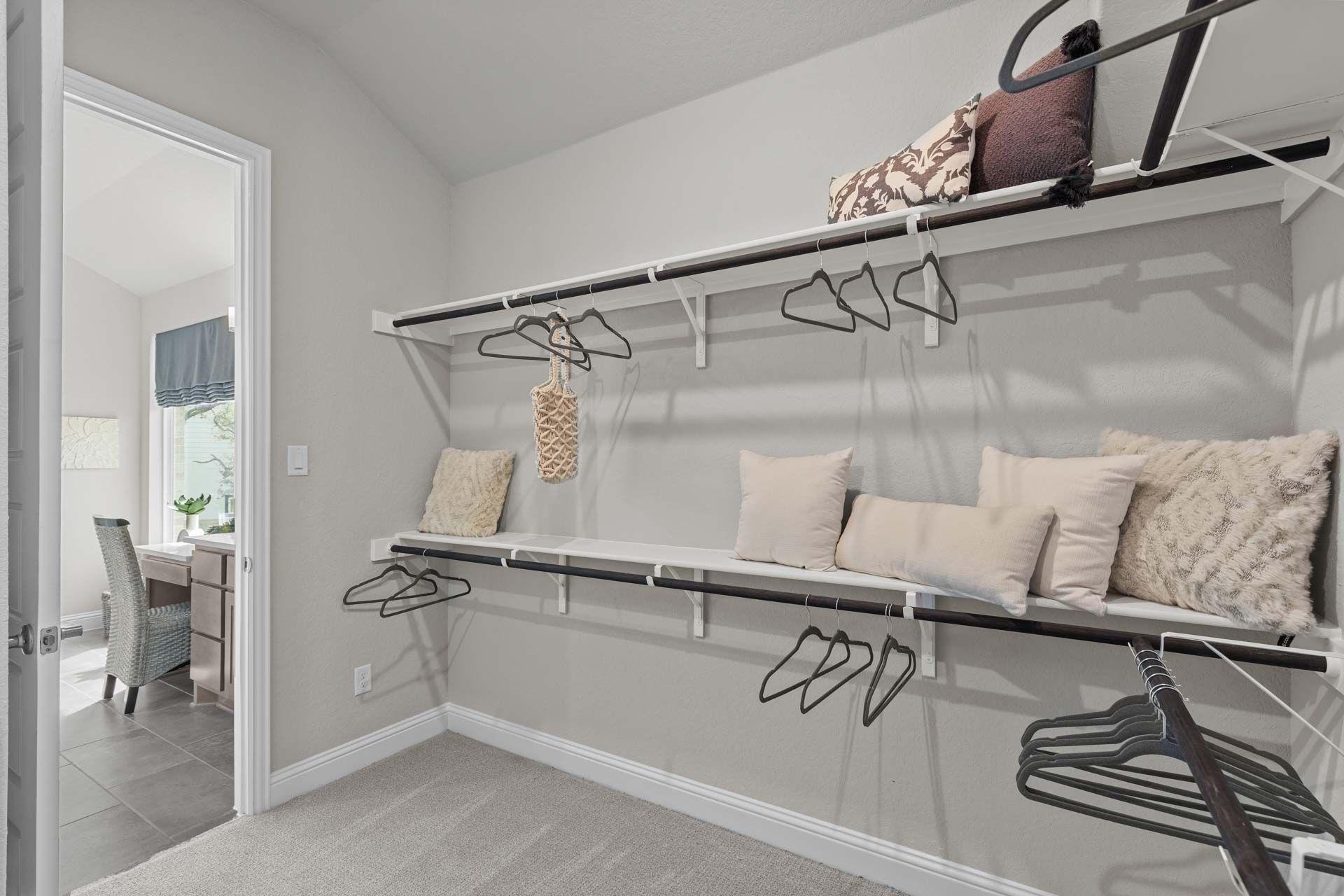 Spacious walk-in closet in Ladera San Antonio home by Davidson Homes with white shelving, hanging rods, pillows, and adjacent office nook
