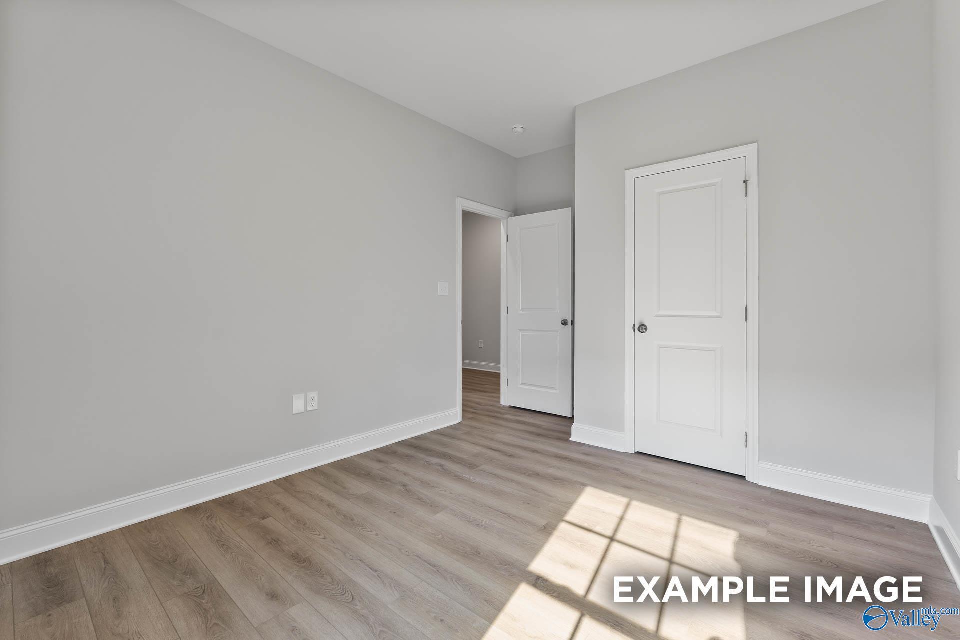Bright empty bedroom featuring light gray walls, white doors, and luxury vinyl plank floors in Davidson Homes The Asheville, Huntsville AL