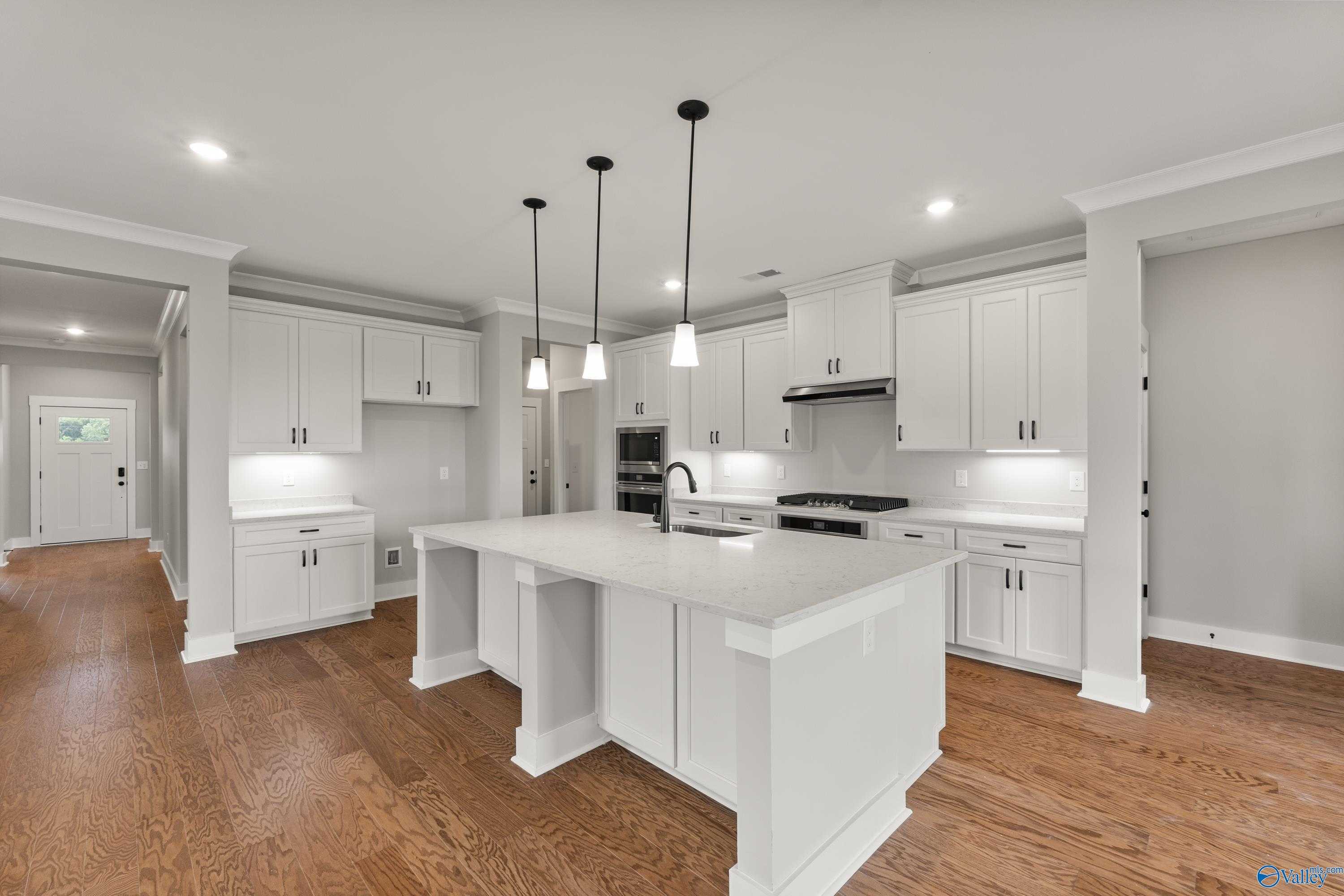 Modern white kitchen with large quartz island, stainless double oven, and pendant lights in The Arcadia home, Huntsville, AL