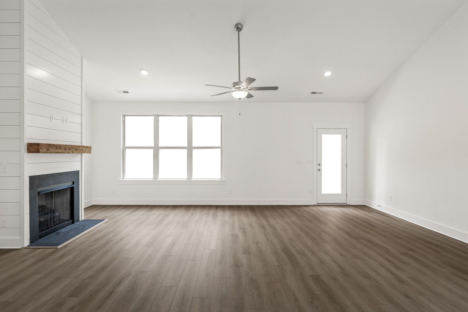 Spacious living room with shiplap fireplace, vaulted ceiling, and luxury vinyl floors in The Ridgeport C at Woods Crossing.