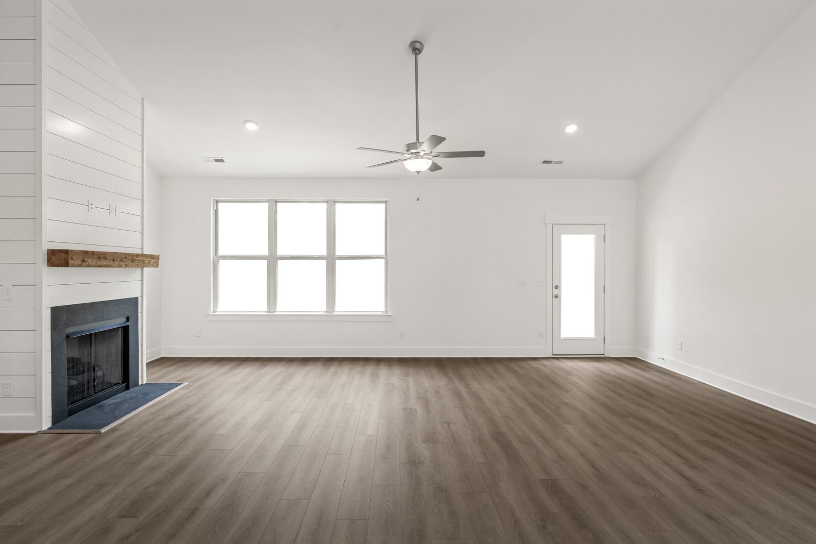 Spacious living room with shiplap fireplace, vaulted ceiling, and luxury vinyl floors in The Ridgeport C at Woods Crossing.