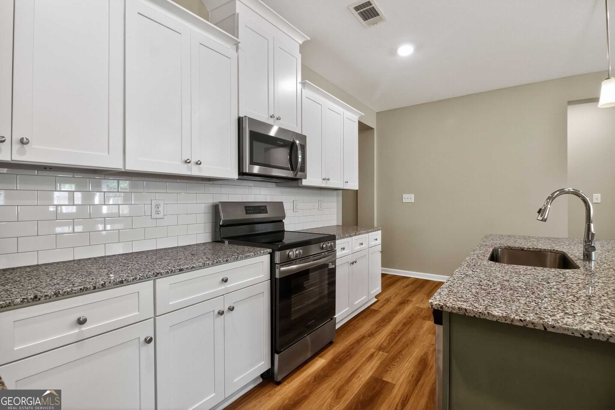 Modern kitchen featuring white shaker cabinets, granite island, stainless appliances, subway tile backsplash in Evermore Homes The Luna, Perry, GA